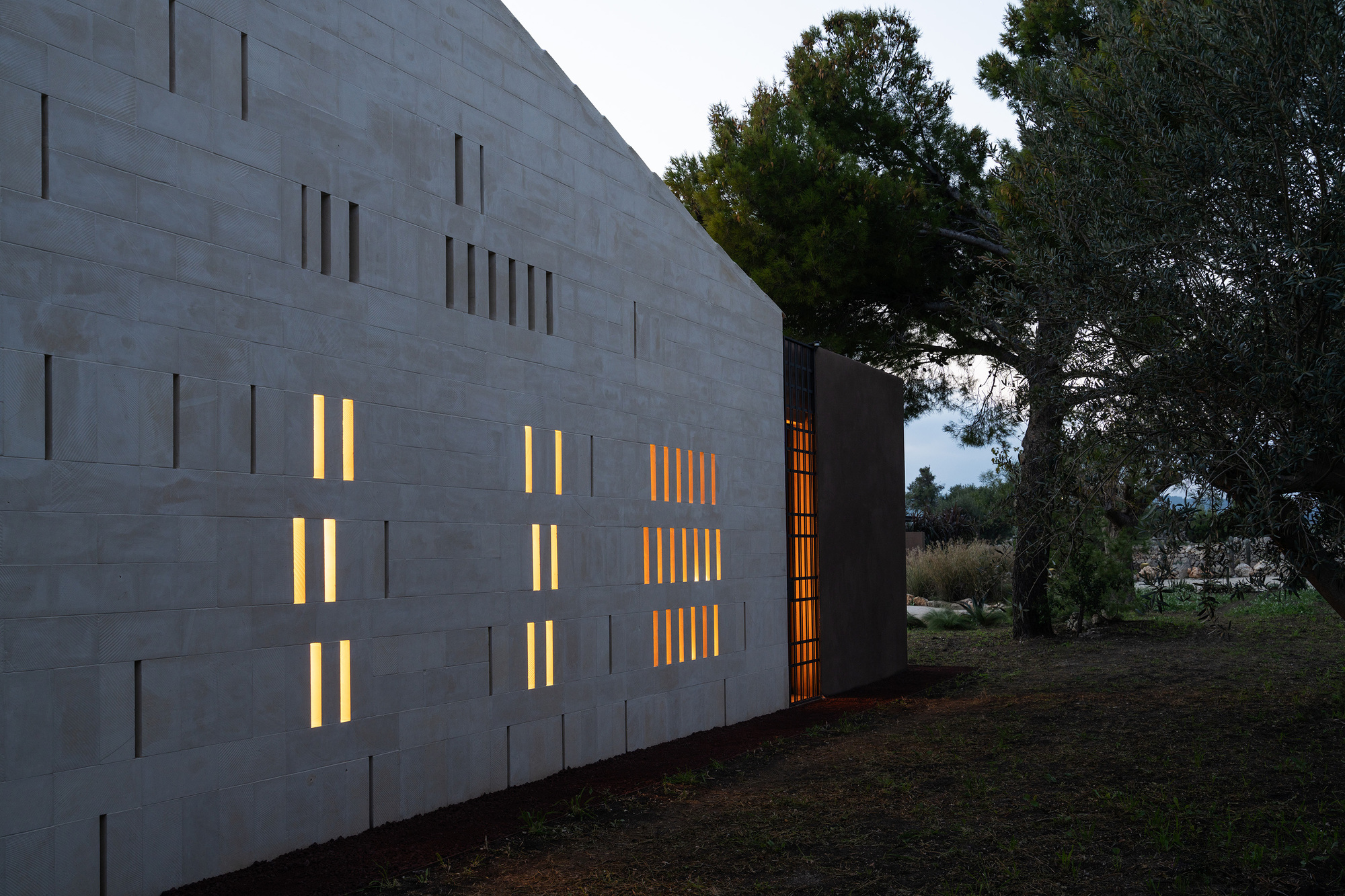 Close-up of the concrete block facade with rhythmic vertical window slits lit from within at dusk