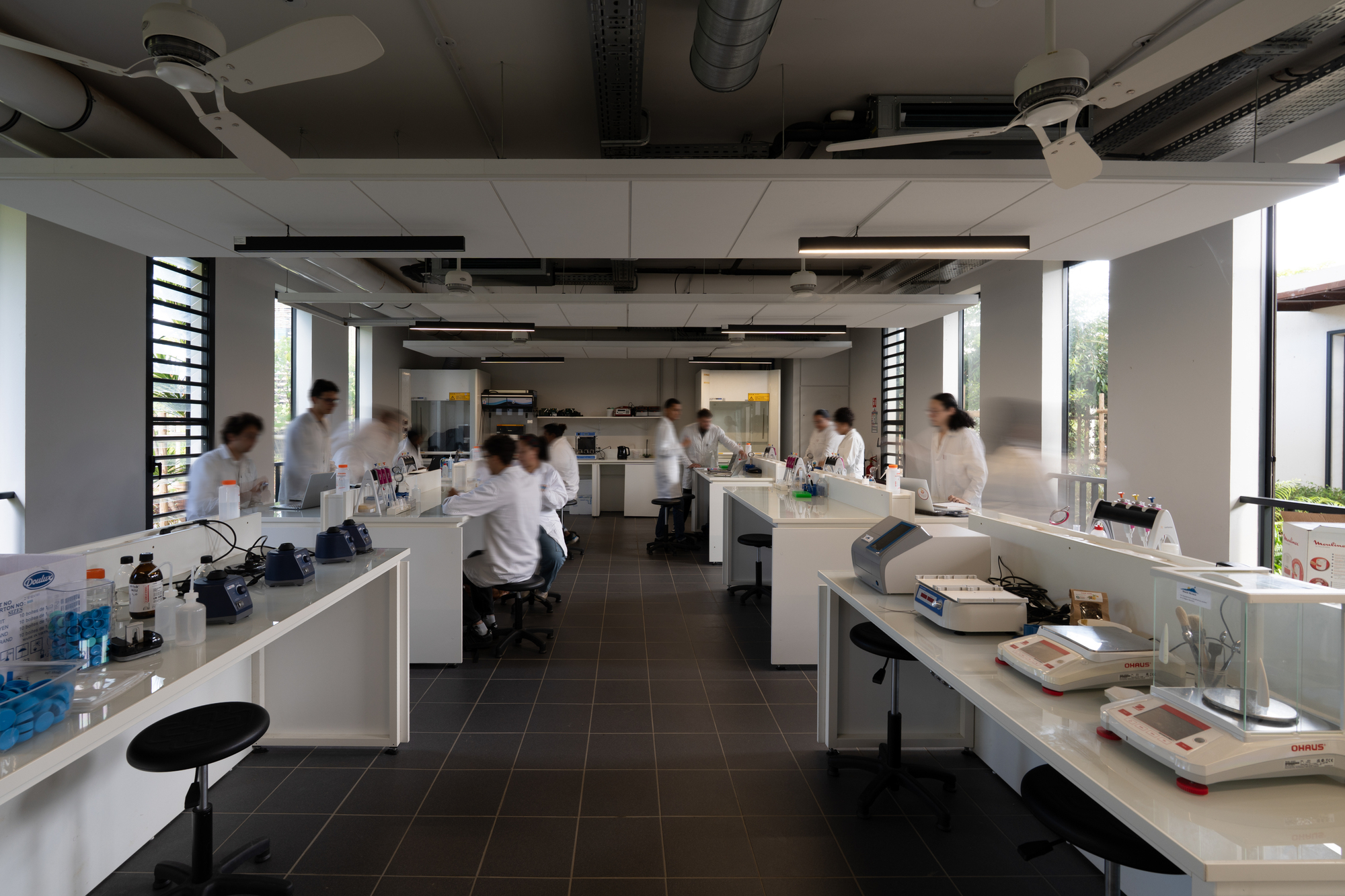 Laboratory interior with white bench islands, exposed ceiling ducts and researchers in white coats at work