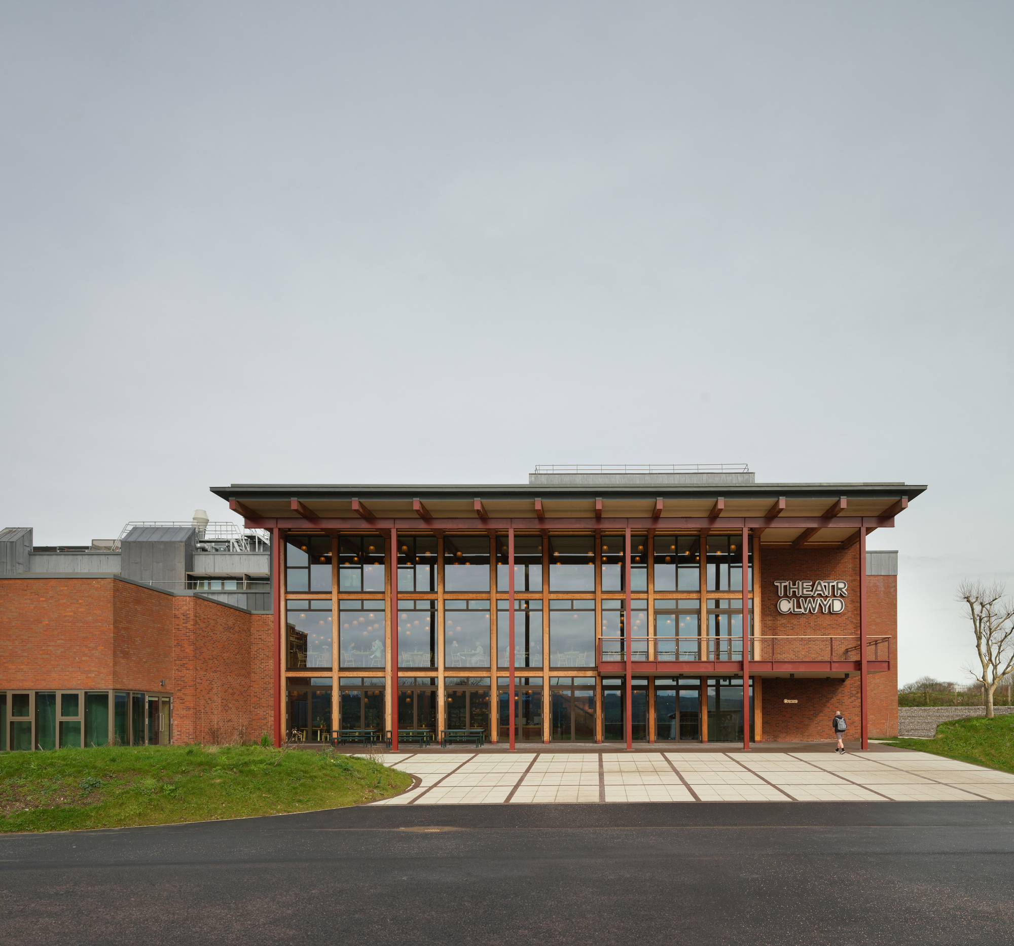 Entrance facade with timber columns and cantilevered roof over glazed curtain wall in overcast light