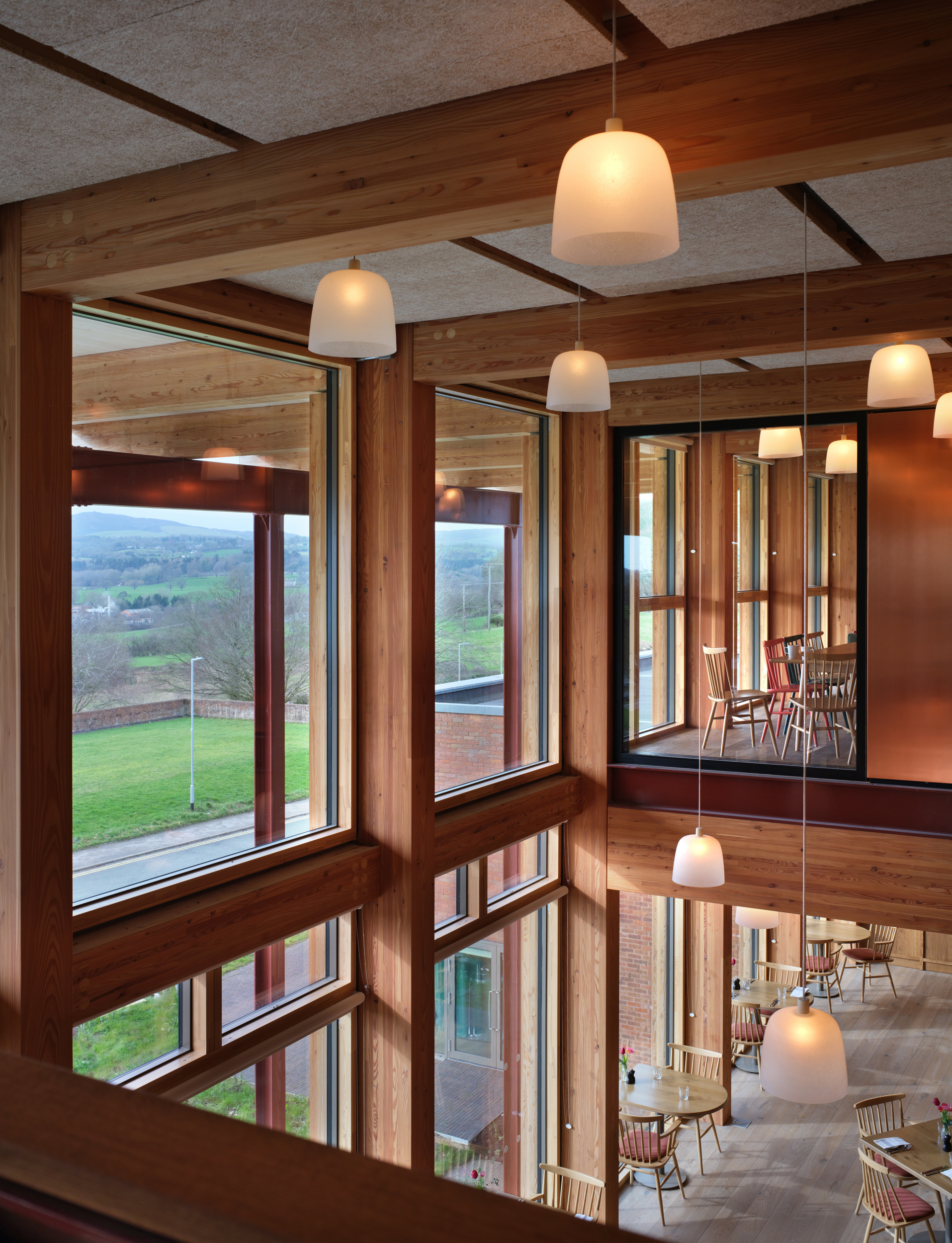 Corner windows framing countryside view with timber mullions and pendant lights reflected in glass