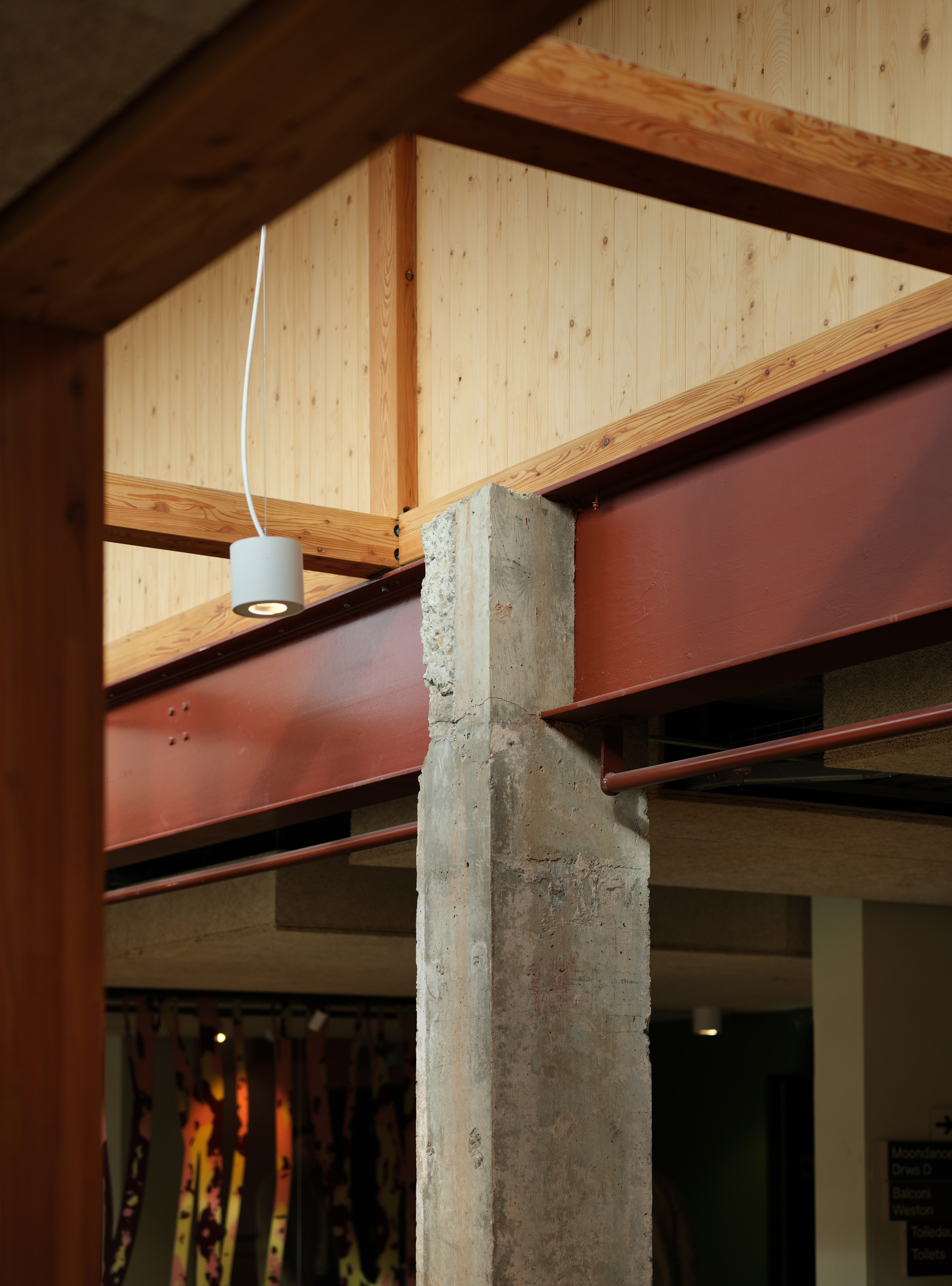Junction detail of concrete column, red steel beam, and timber roof structure with pendant light
