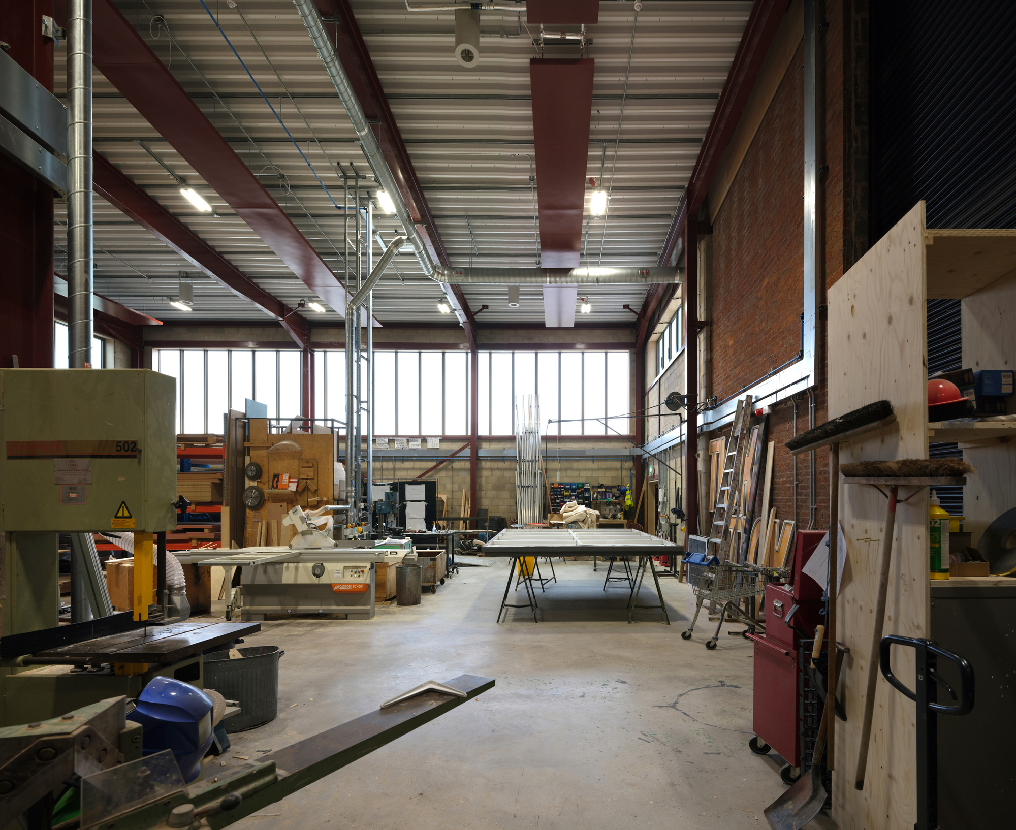 Workshop interior with exposed steel beams, corrugated metal ceiling, and worktables surrounded by tools and materials