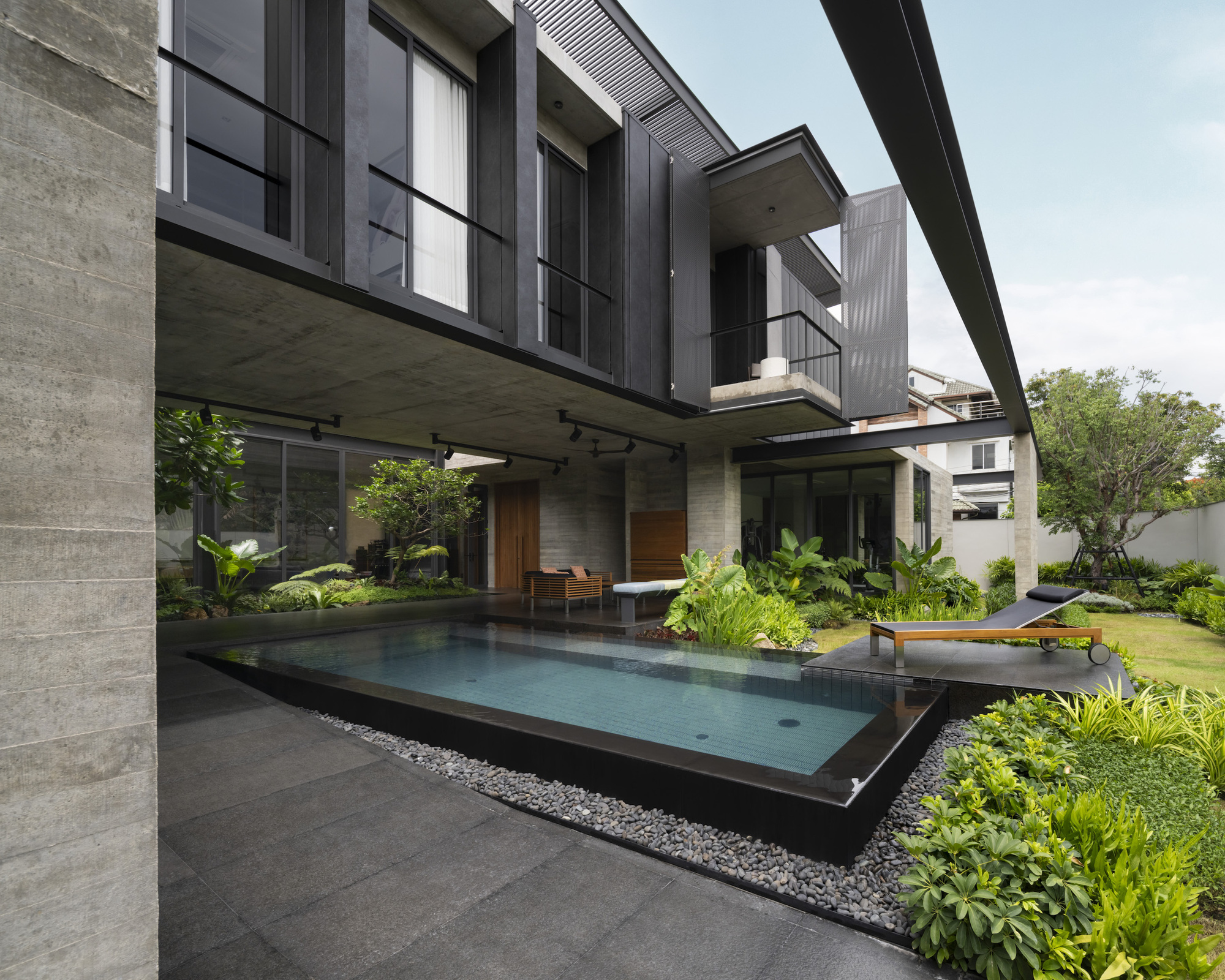 Garden courtyard showing the elevated dark volume cantilevering over the pool and terrace below