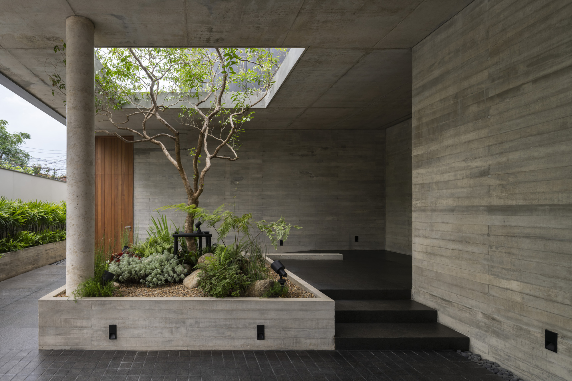 Covered entry terrace with planted bed containing a specimen tree under a concrete skylight