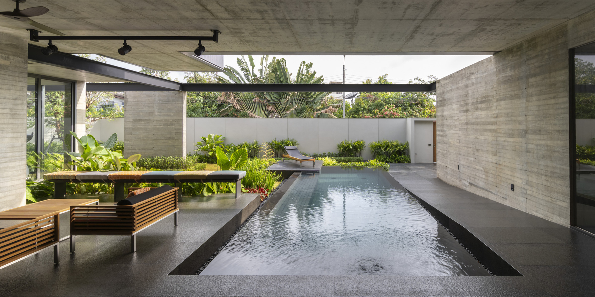 Covered courtyard with rectangular swimming pool and board-formed concrete walls framing tropical planting