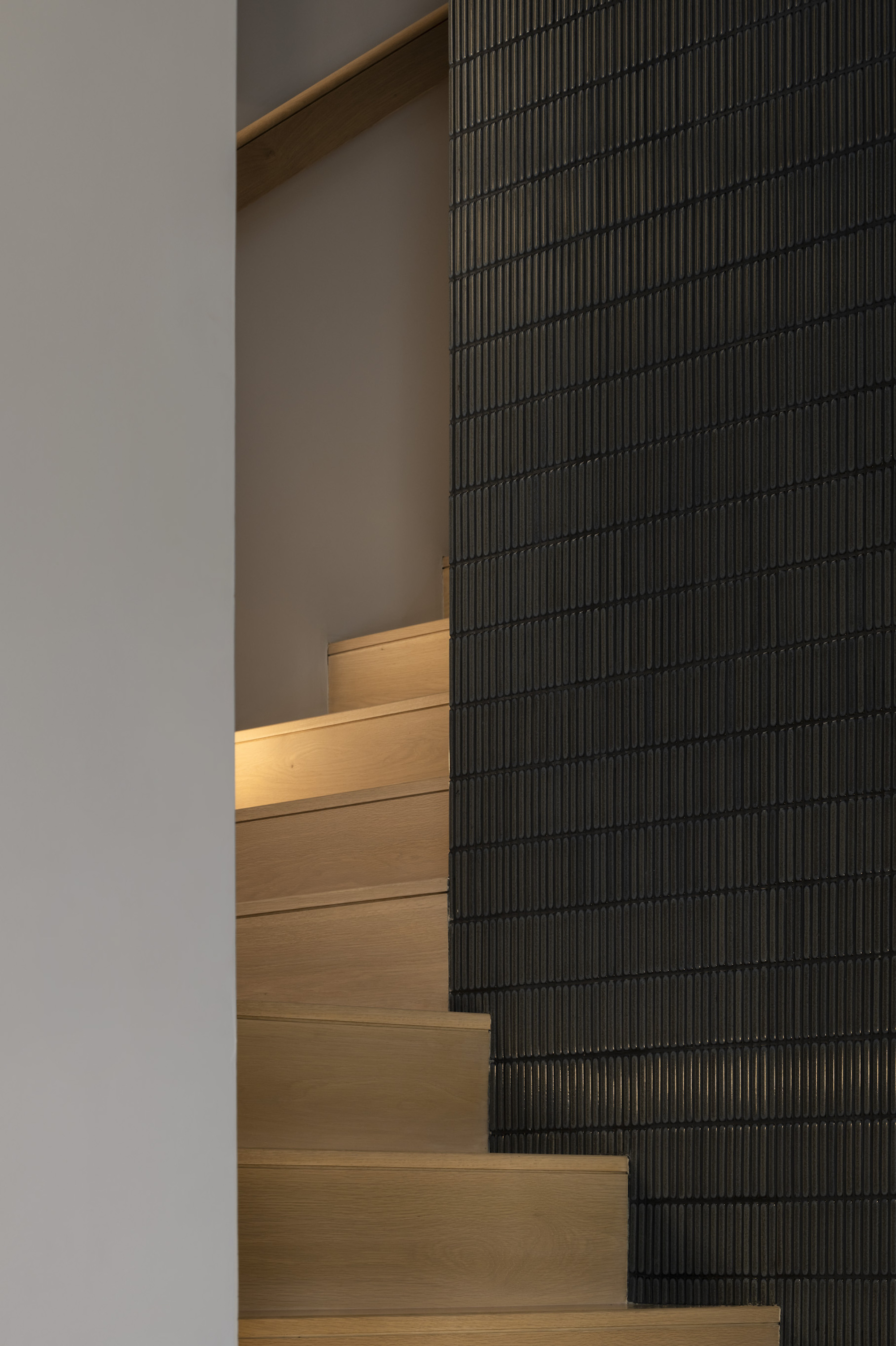 Timber staircase with integrated lighting alongside a black ribbed tile wall
