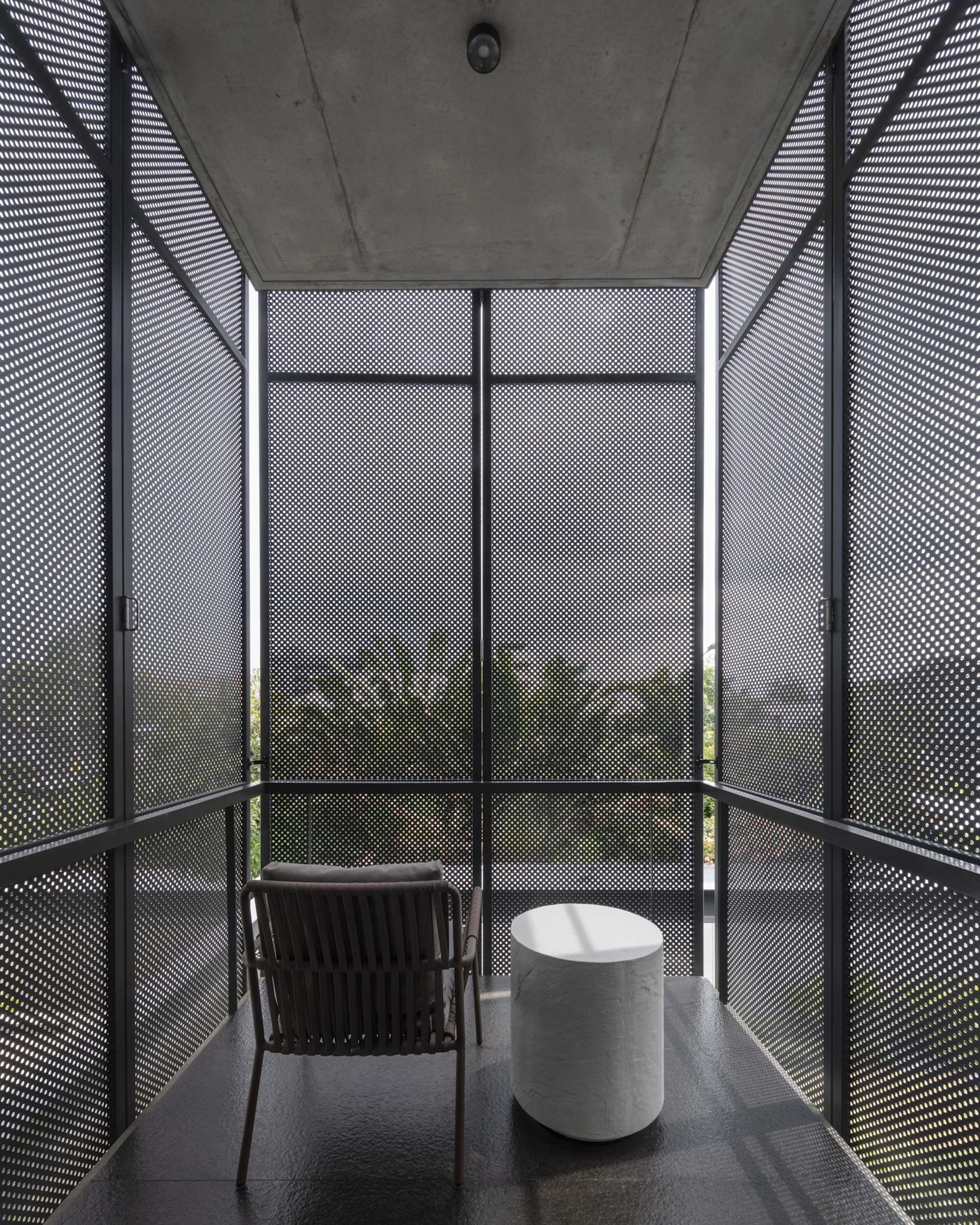 Enclosed balcony with perforated metal screens and exposed concrete ceiling at dusk