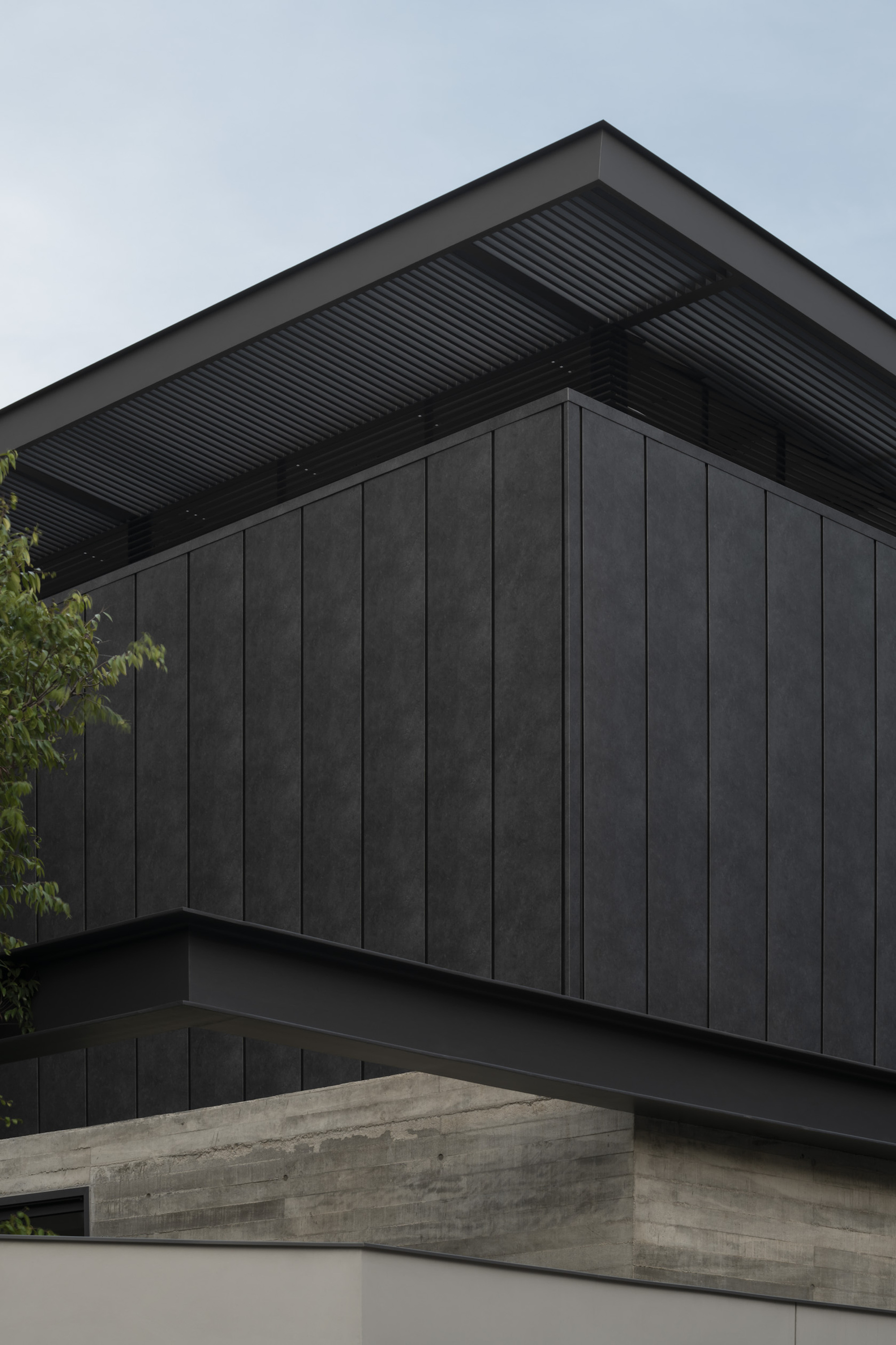 Corner detail of dark timber cladding with corrugated metal soffit and board-formed concrete wall below