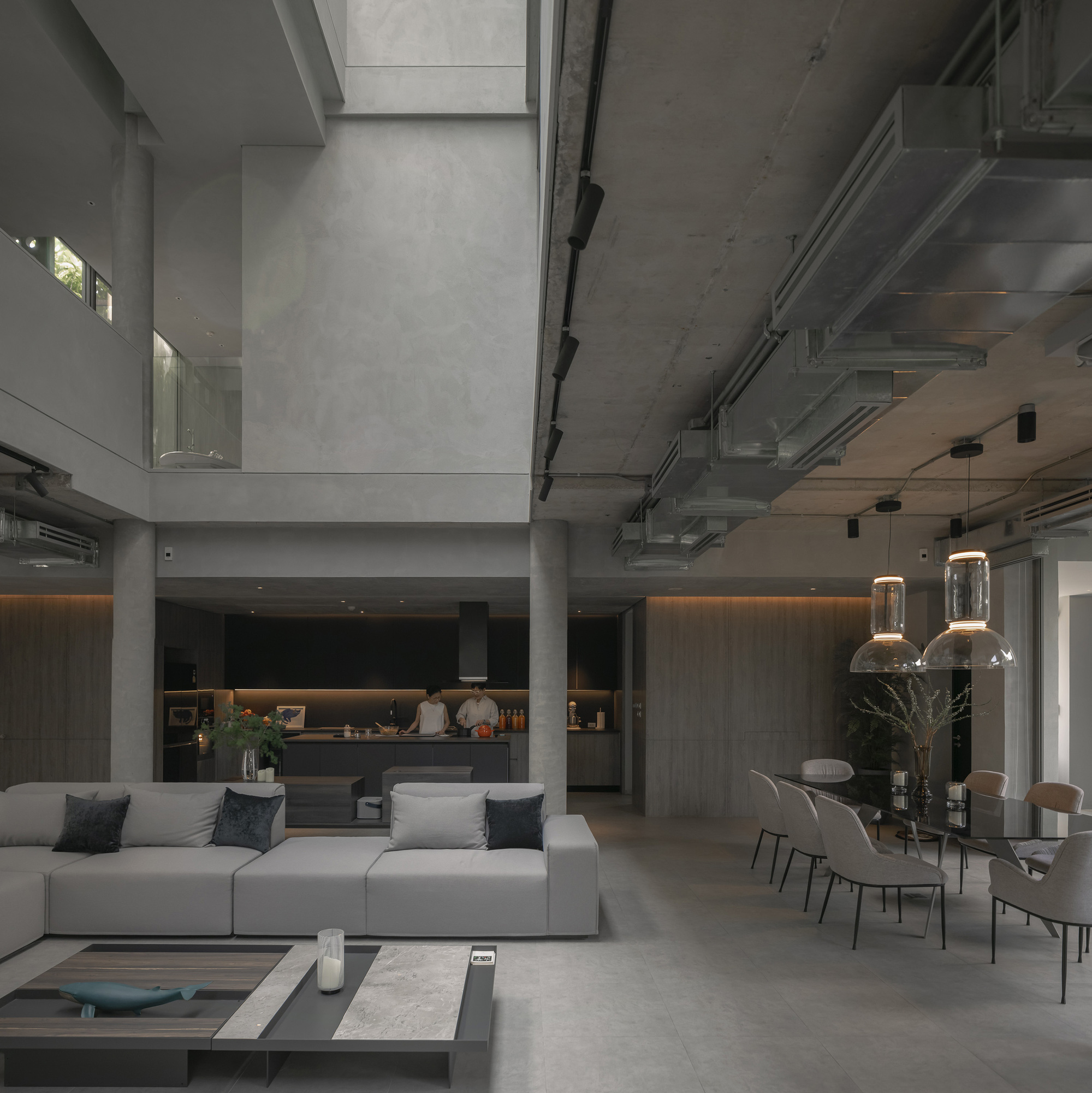 Open-plan living area with exposed concrete ceiling, pendant lights, and a kitchen beyond