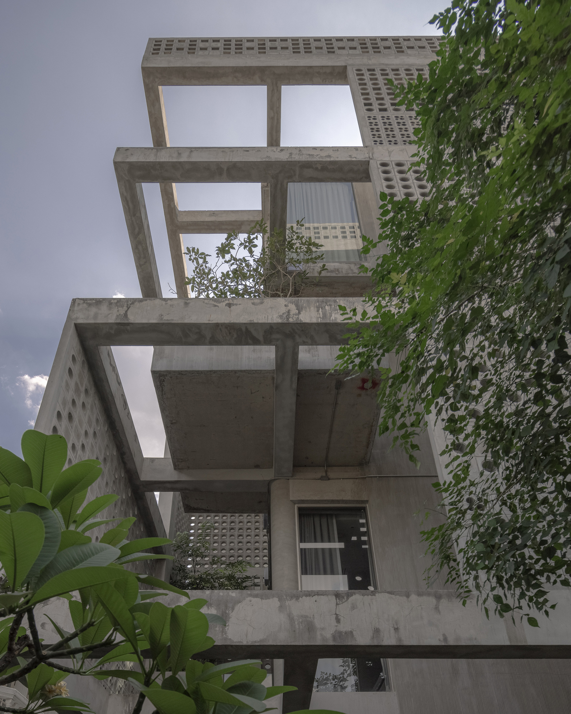 Stacked concrete terraces with perforated screens and planted balconies framed by banana leaves