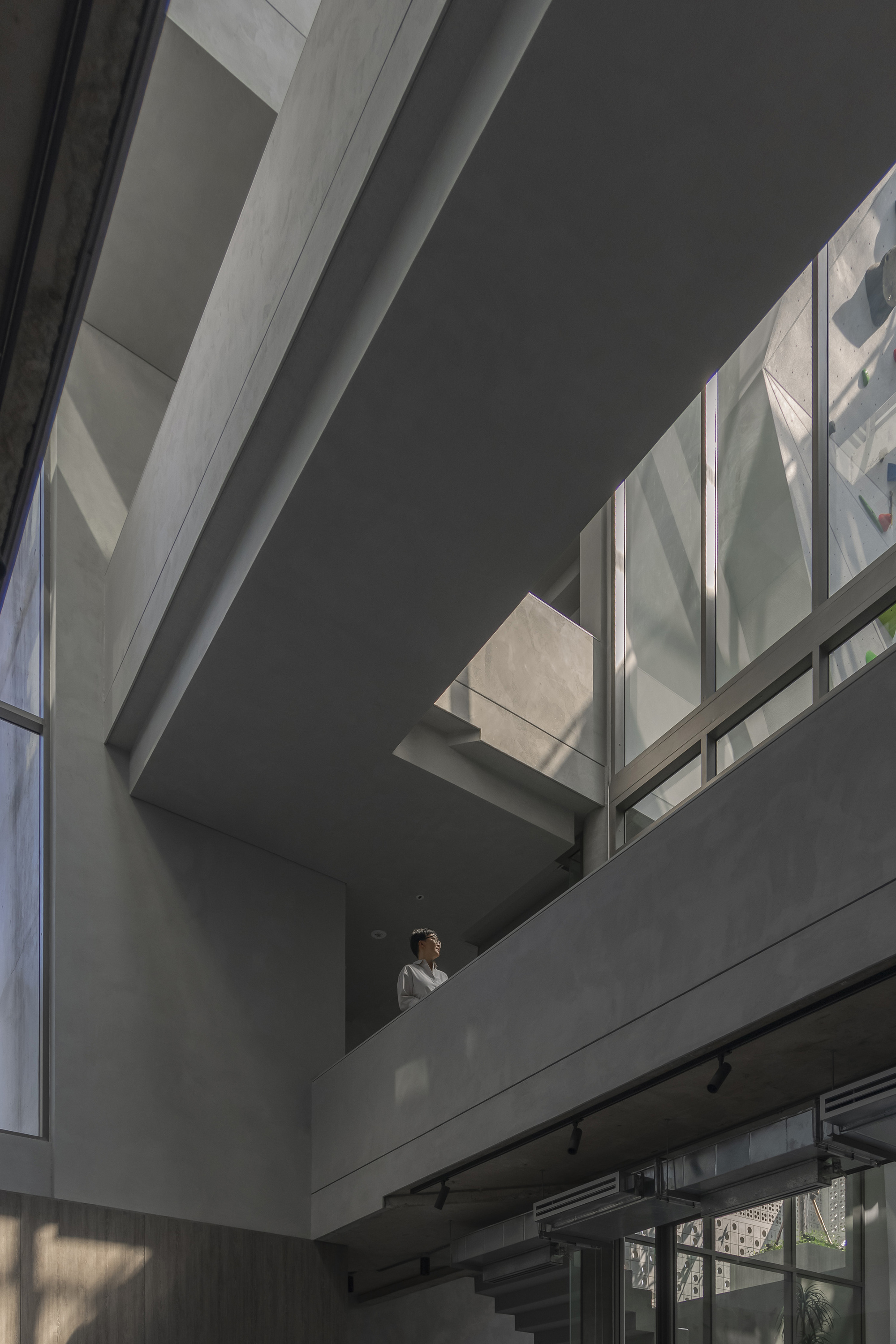 Interior atrium view showing overlapping concrete balconies with a single person standing in dappled sunlight