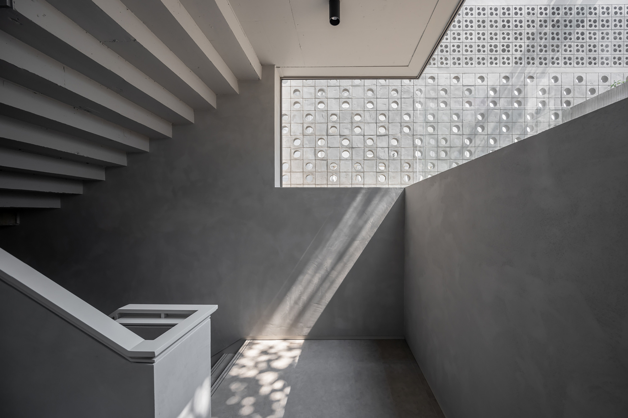 Stairwell landing with horizontal louvered wall and perforated screen visible through skylight above