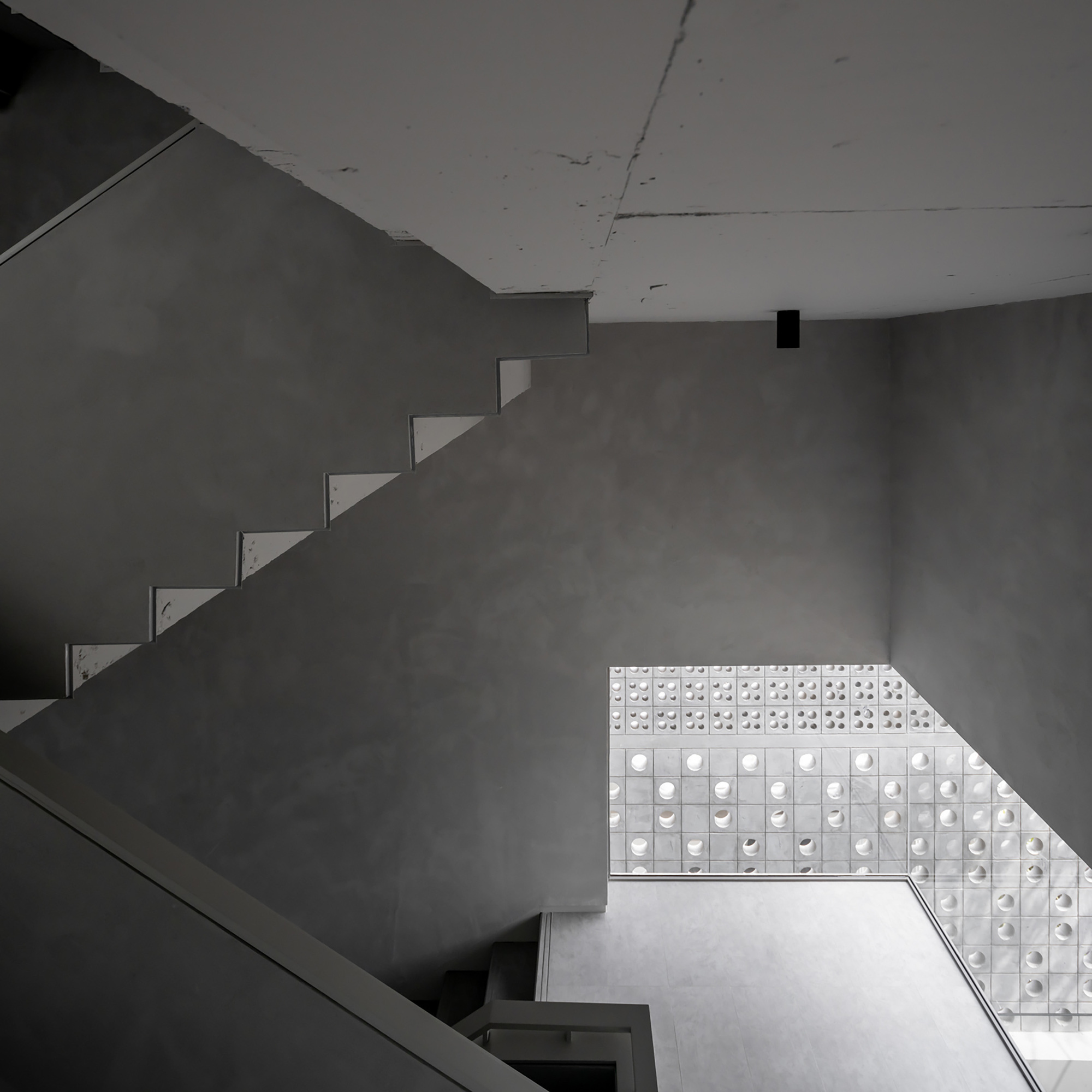 Looking up at cantilevered concrete stairs against a perforated glass block wall filtering natural light