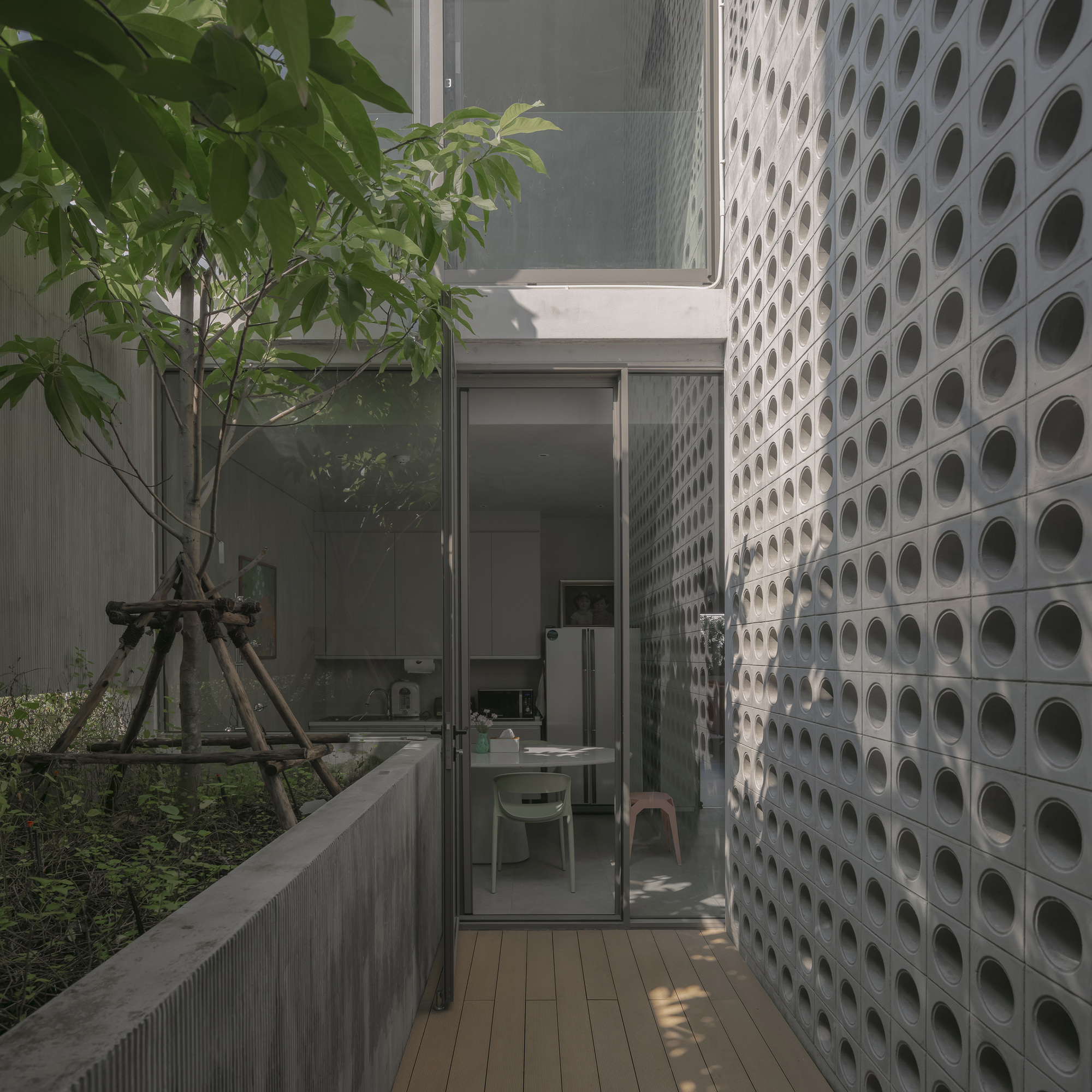 Timber deck corridor alongside perforated concrete block wall with young tree in planted bed