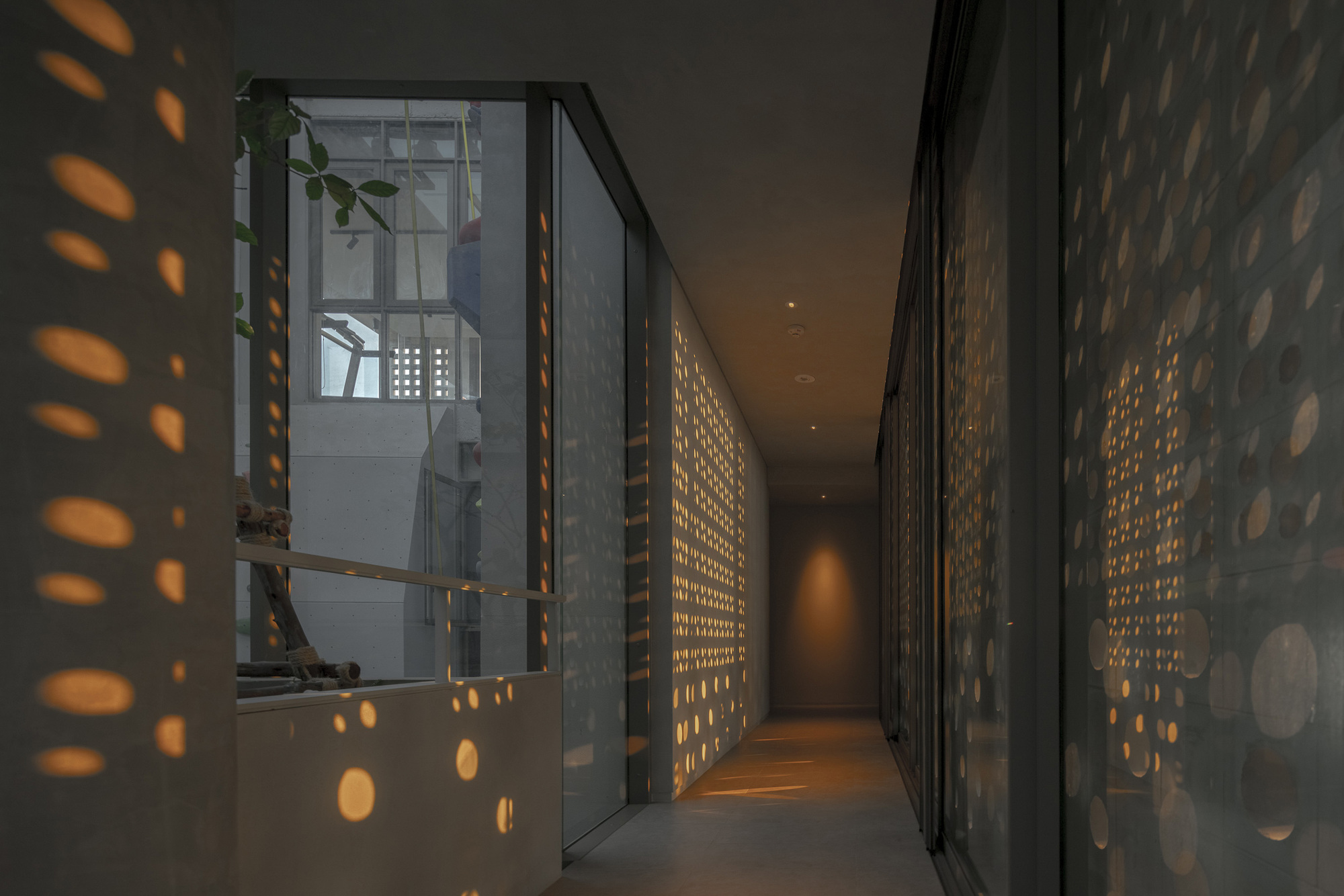Interior corridor at dusk with perforated screens casting oval light patterns on walls and floor