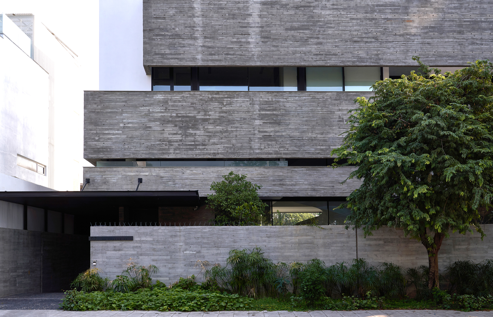 Entry facade showing layered concrete volumes with a cantilevered upper floor and planted foreground