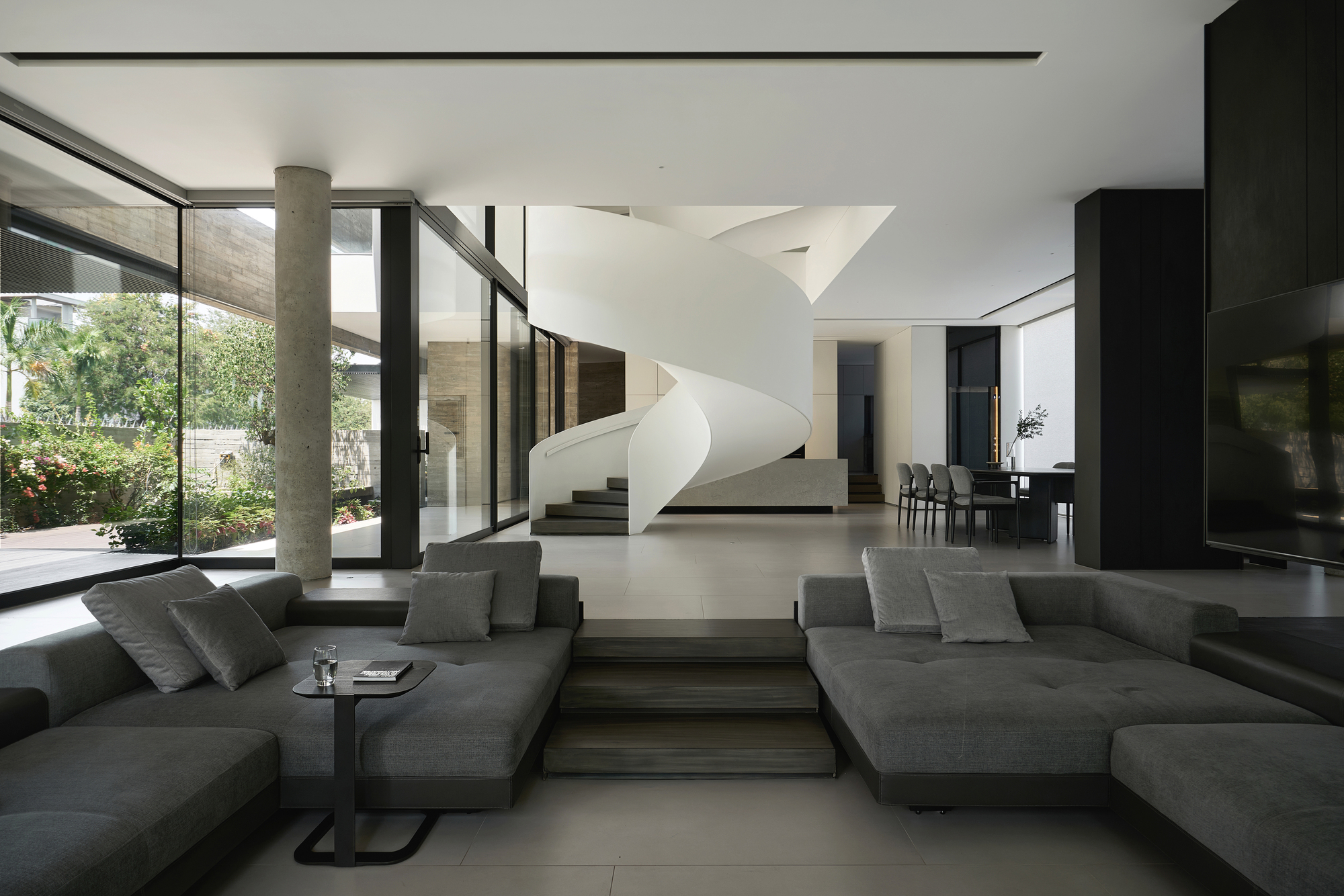Double-height living room with a white helical staircase and floor-to-ceiling glass overlooking the garden