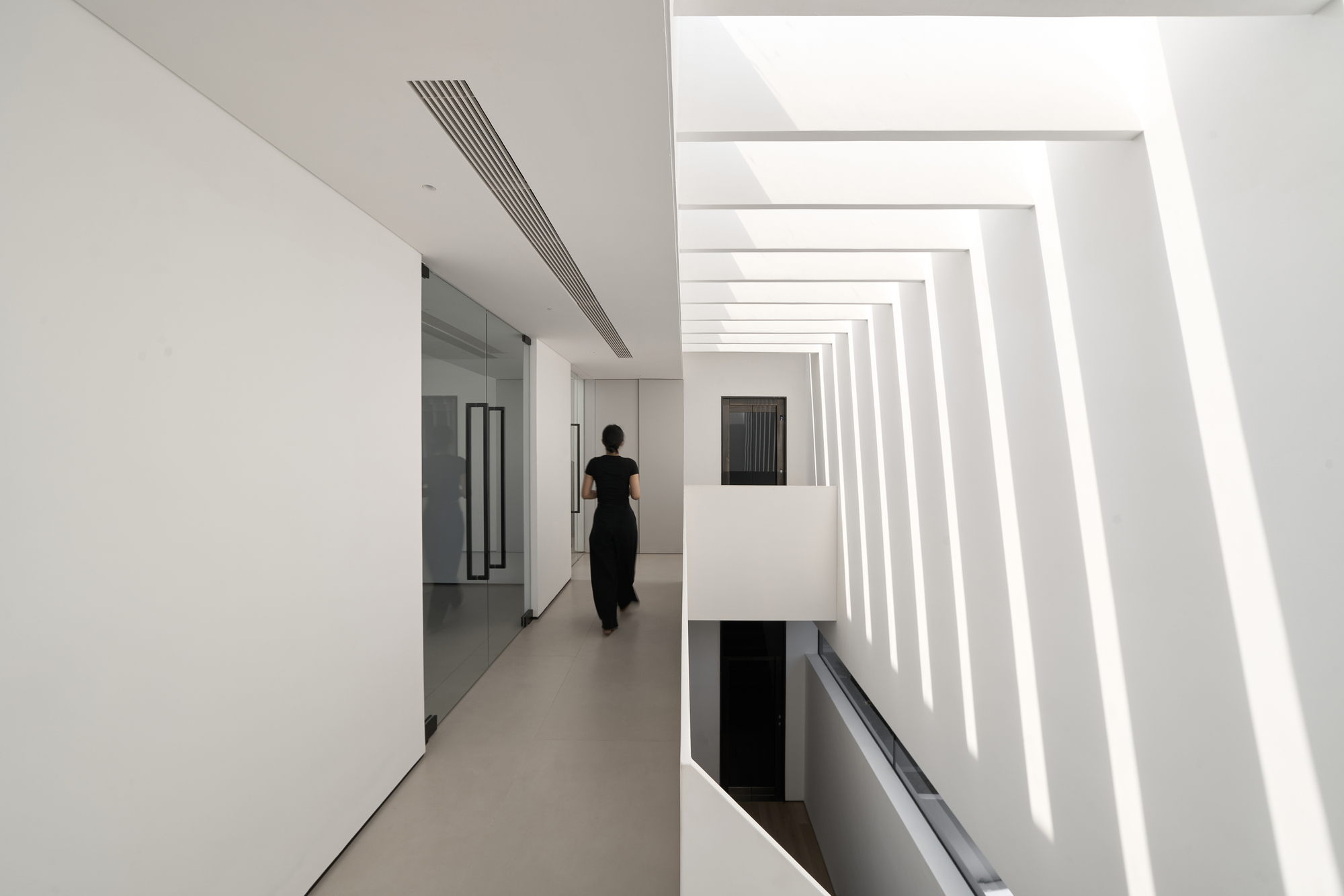 Upper hallway with recessed linear lighting and a person walking past a stair void