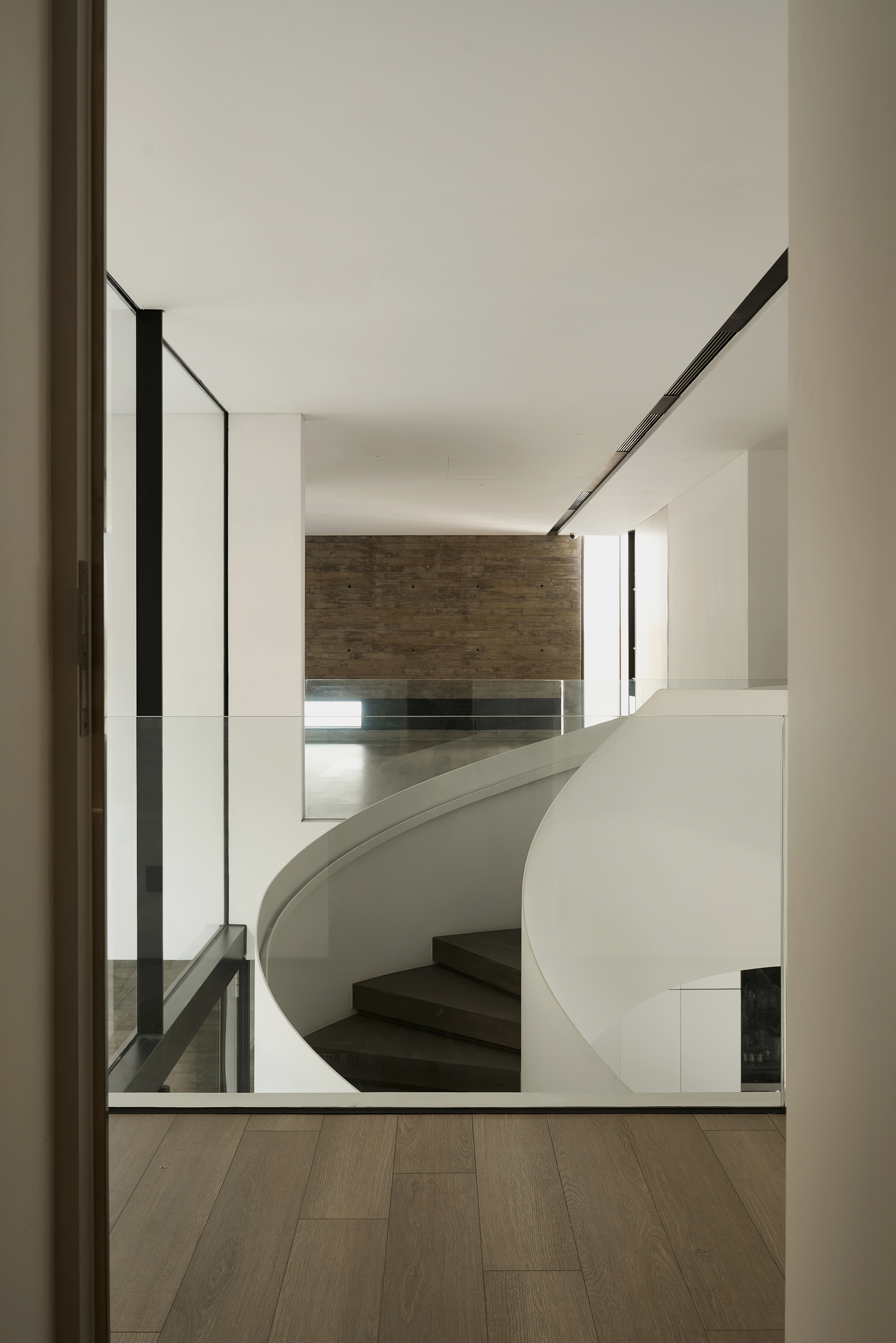 View through a doorway to the curved white staircase descending toward a timber-clad wall