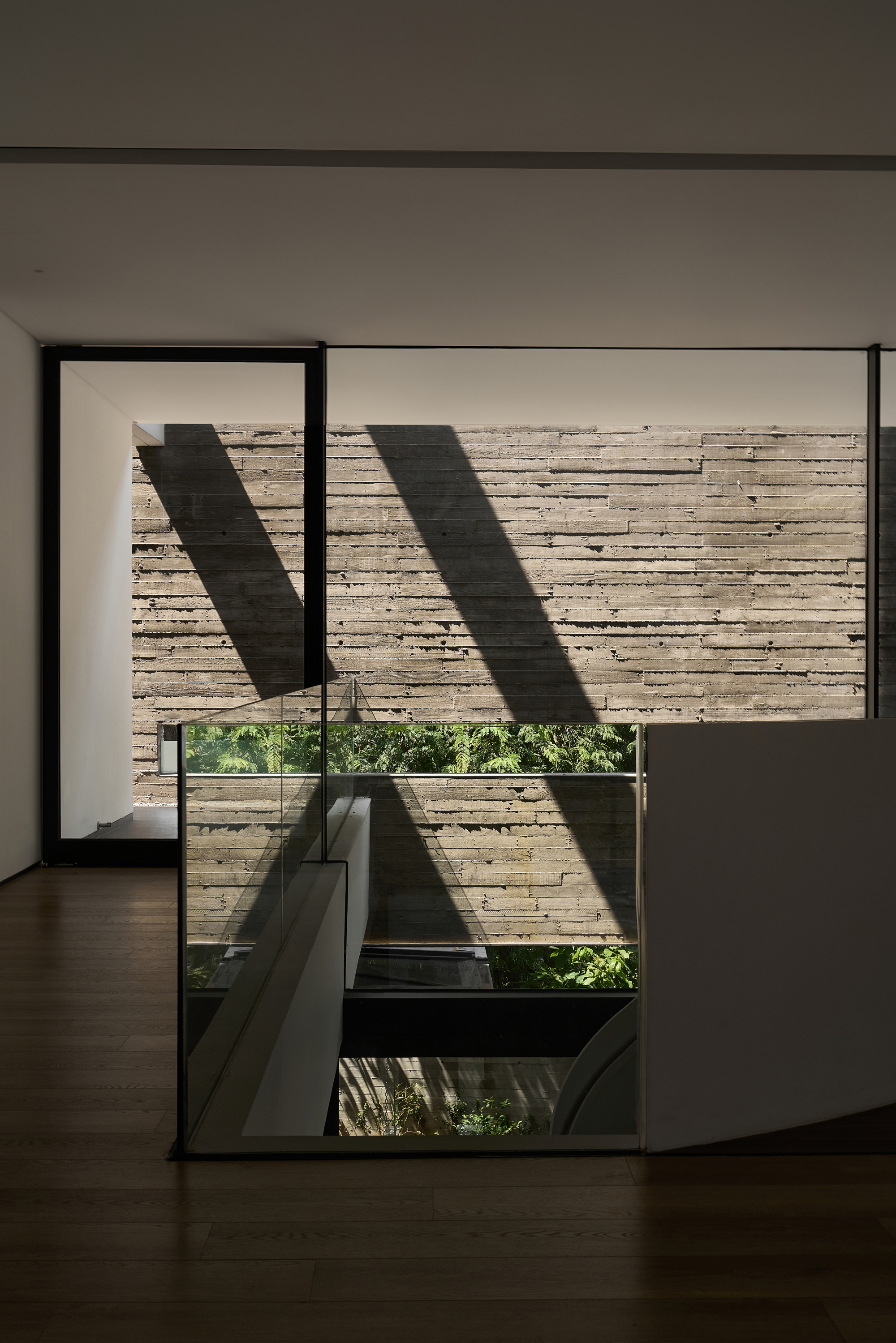 Floor-to-ceiling window framing a board-formed concrete wall with angular shadows from above