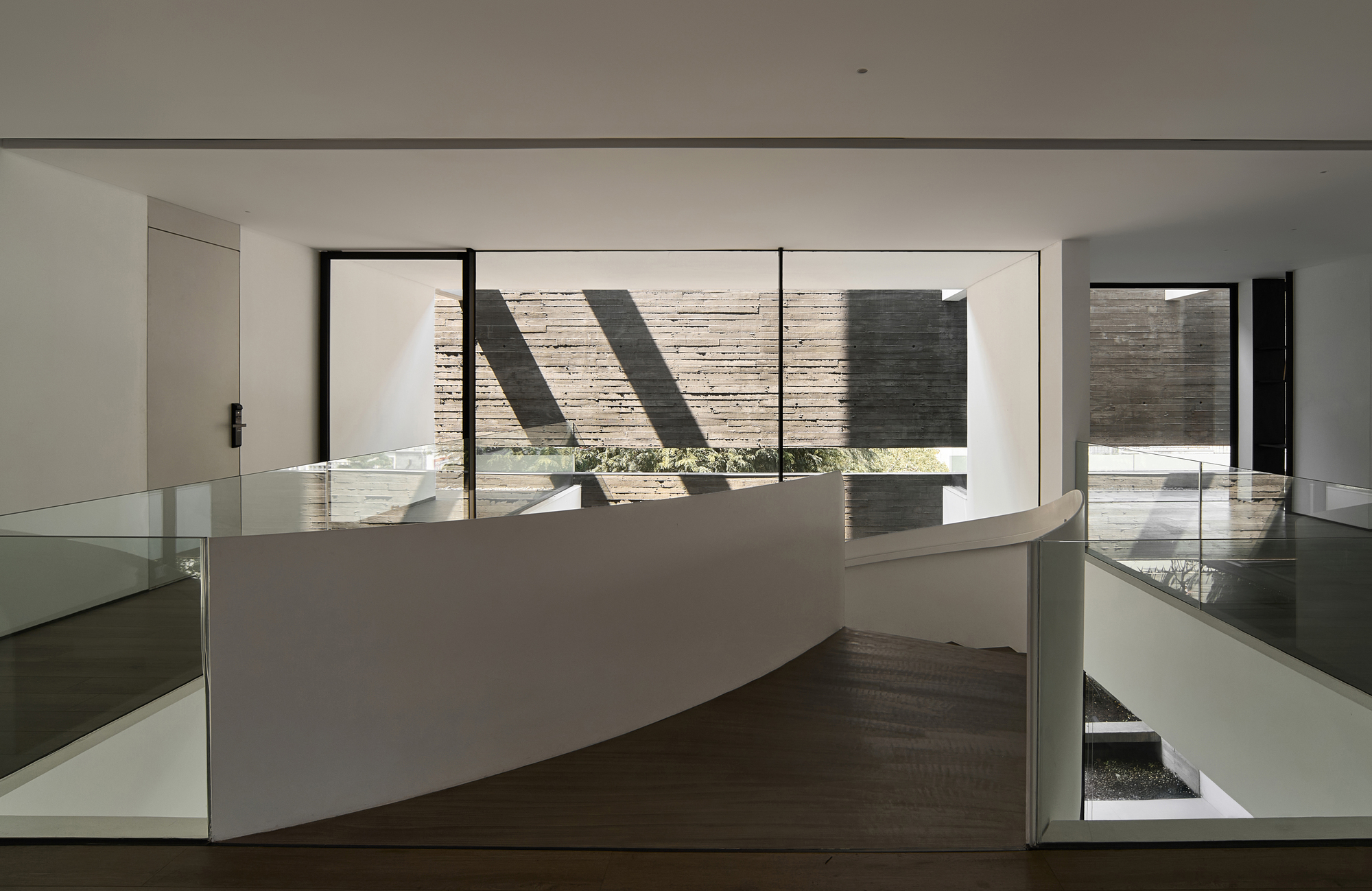 Upper landing with curved glass balustrade overlooking a courtyard through large windows