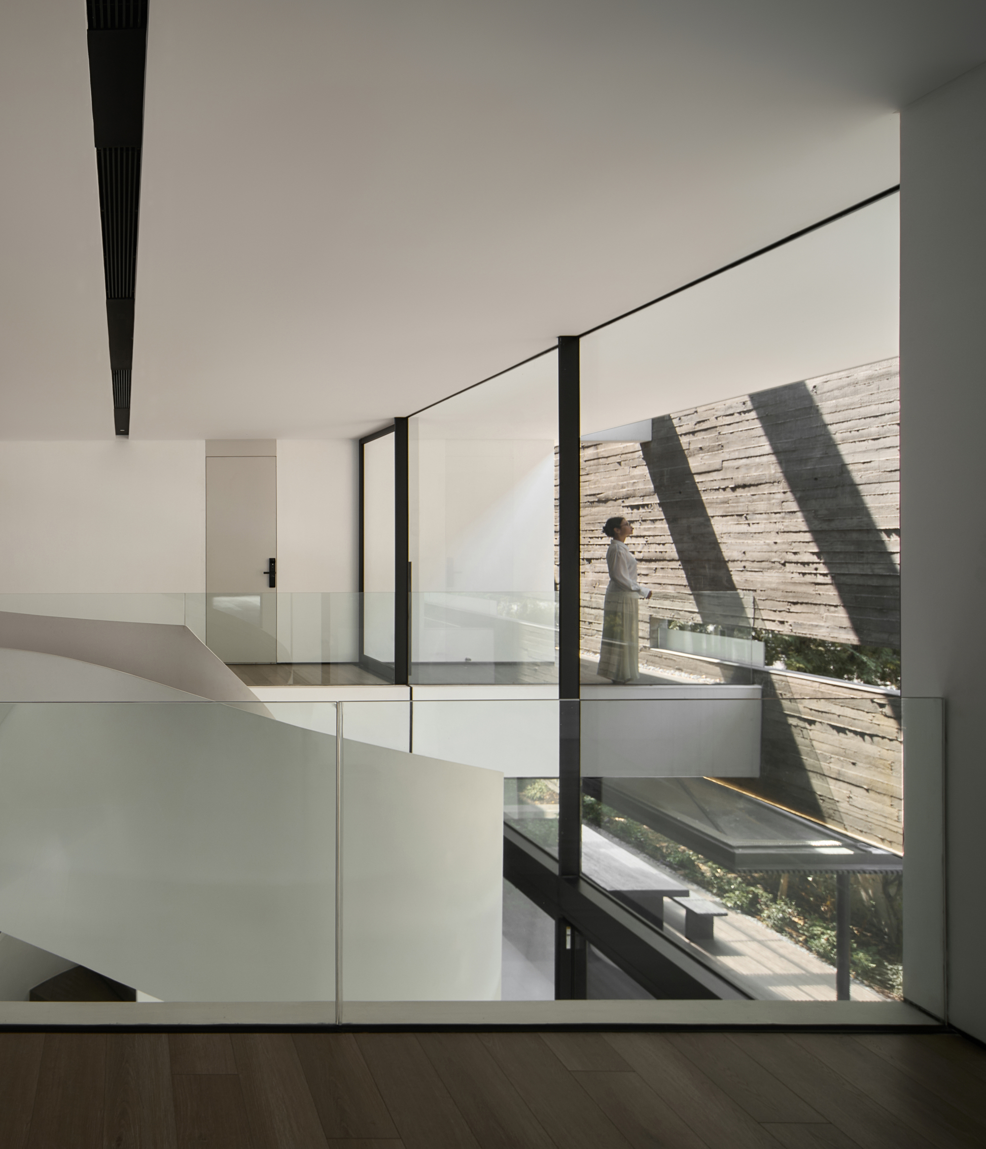 Interior hall with a figure walking past full-height glazing onto a courtyard terrace