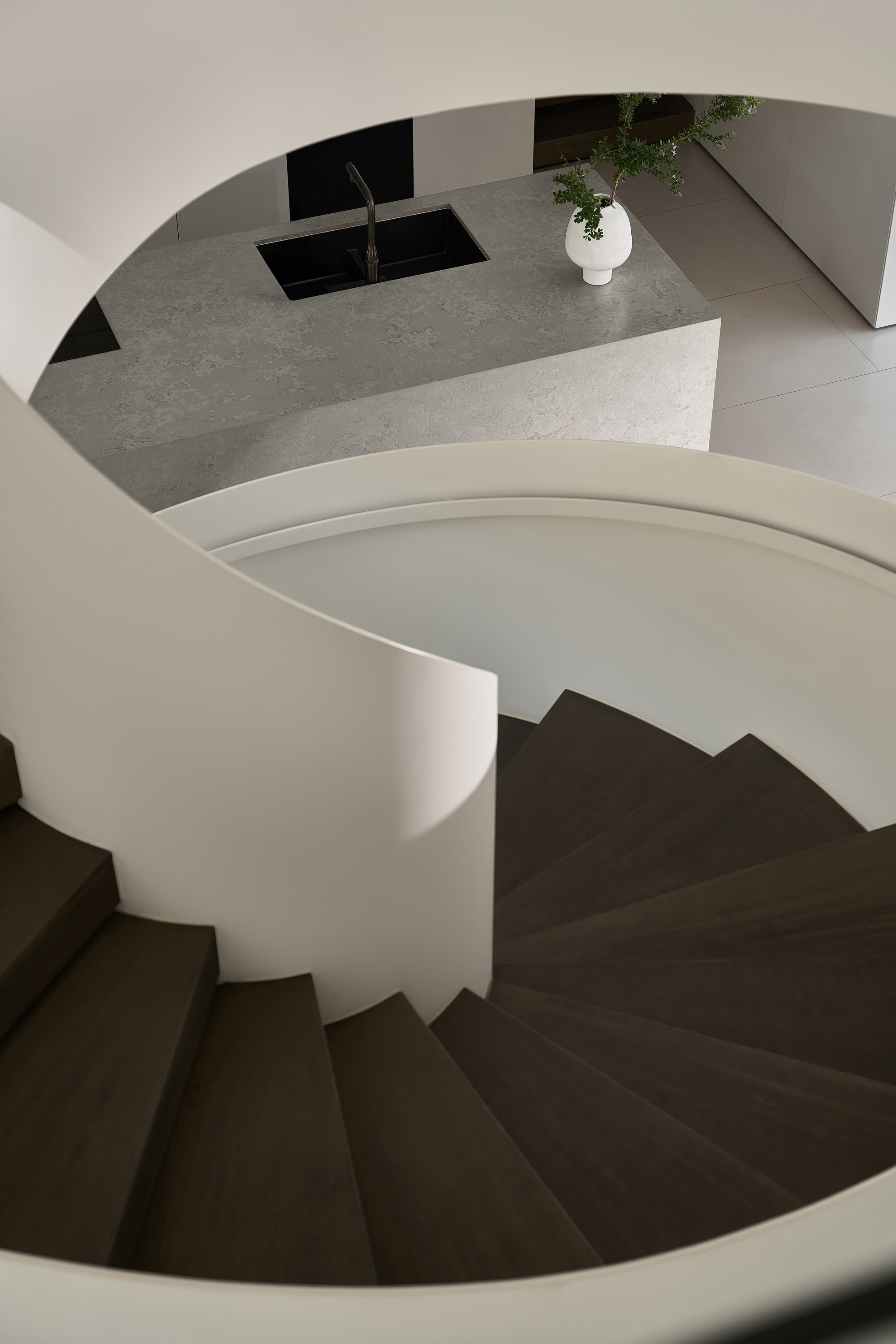 Top-down view of spiral staircase with dark treads and terrazzo island visible above
