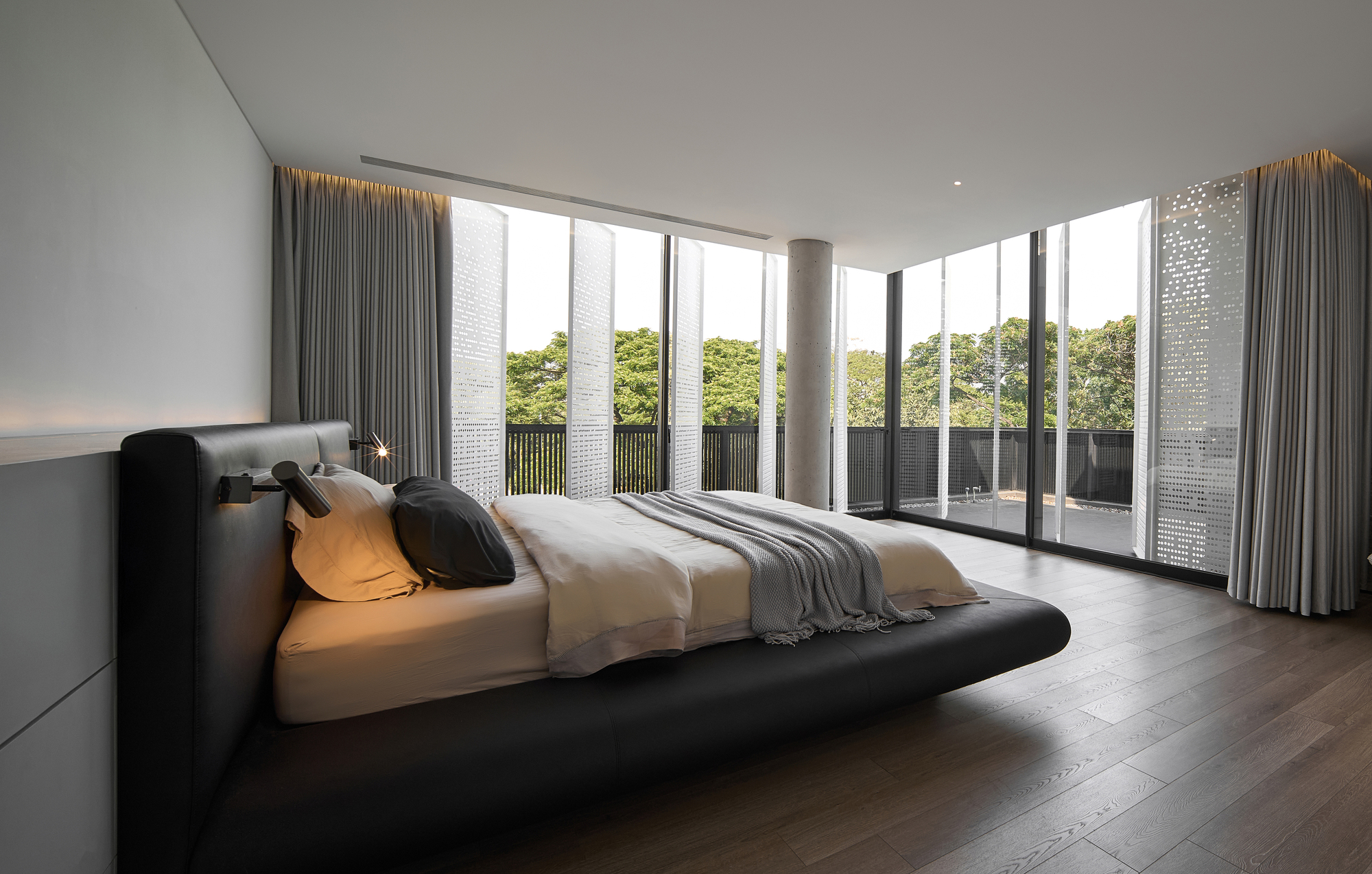 Corner bedroom with floor-to-ceiling glass walls overlooking greenery and grey curtains filtering daylight