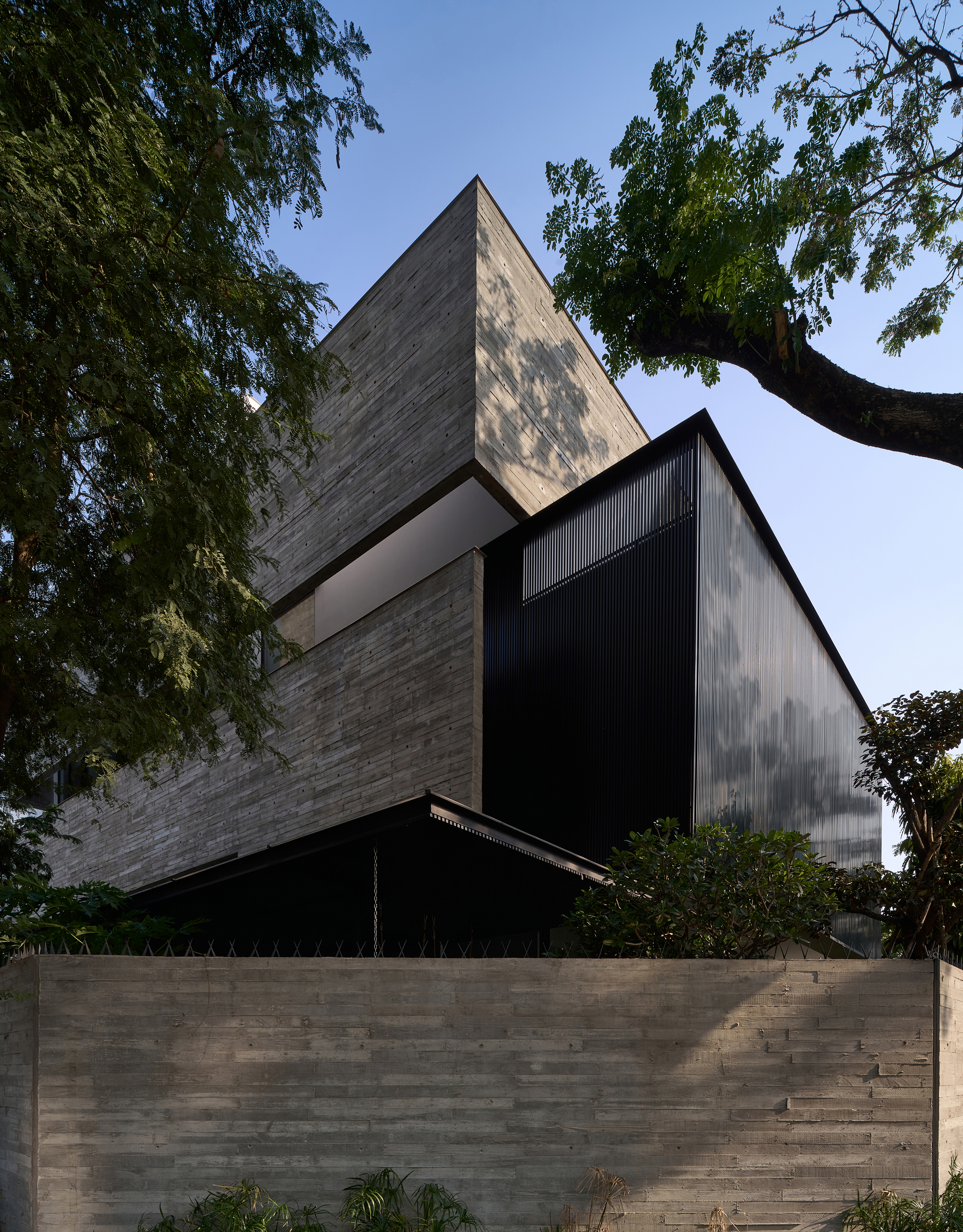 Stacked volumes clad in board-formed concrete and black metal beneath overhanging tree branches