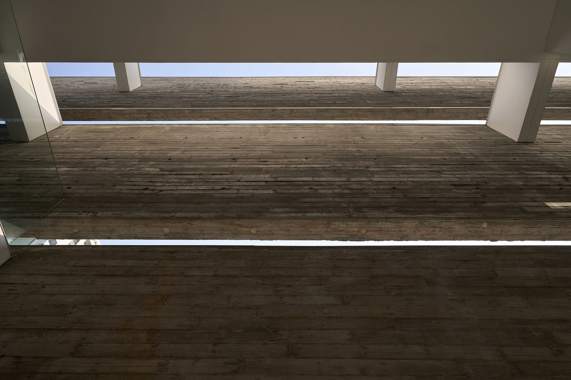 Upward view of timber bridge spanning between volumes under continuous skylight strips