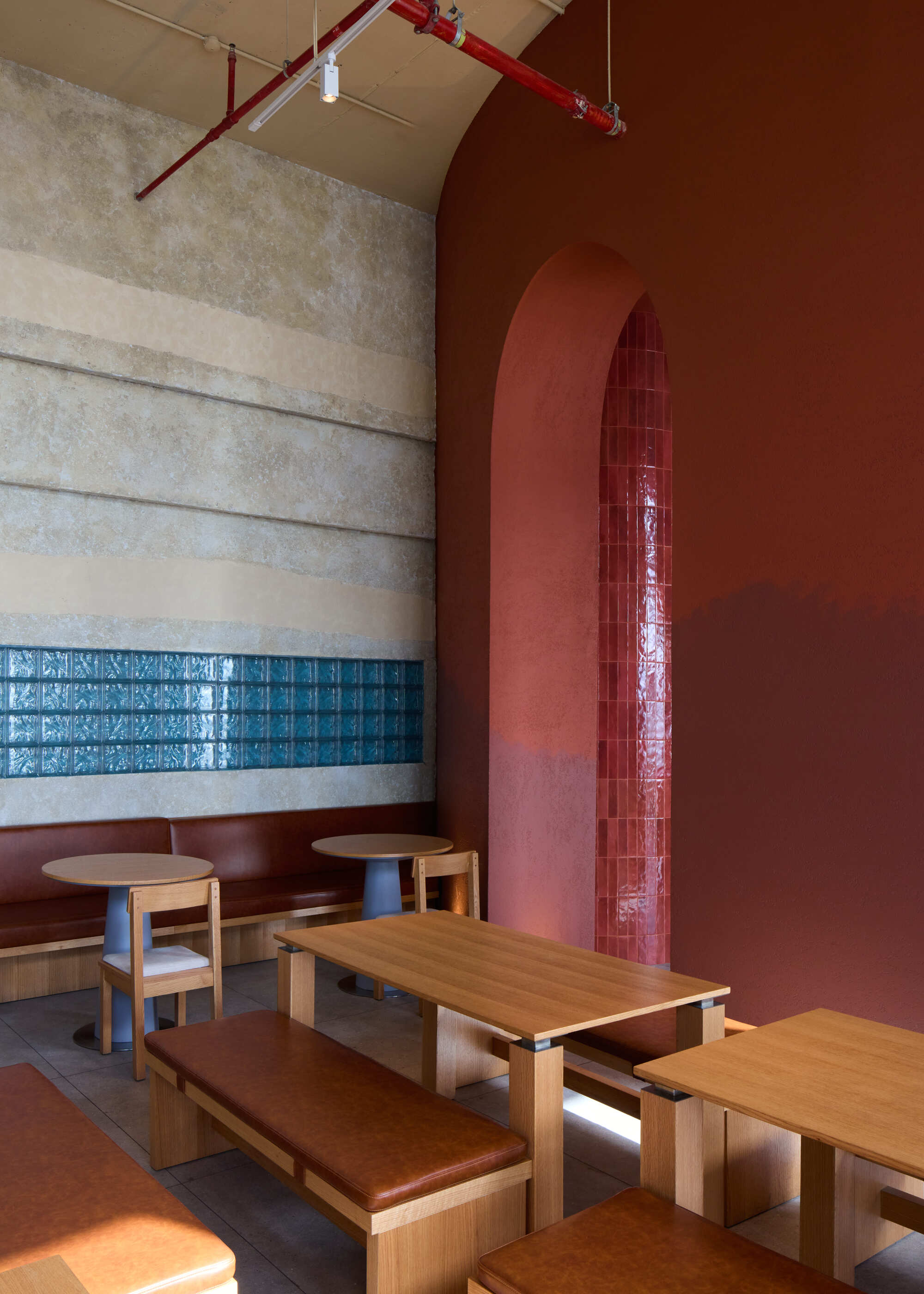 Corner detail of arched alcove with red glazed tile niche beside timber benches and exposed red conduit