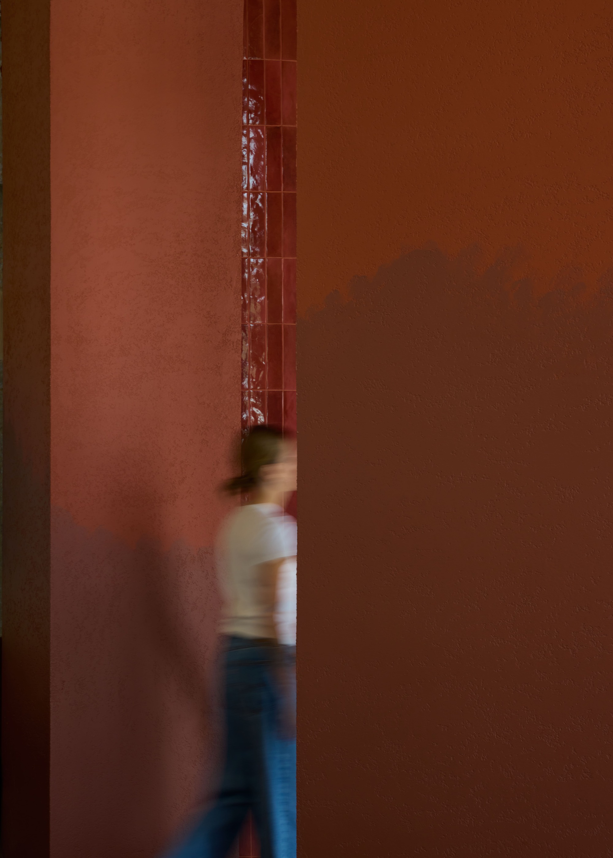 Narrow passageway with terracotta walls and a blurred figure in motion walking through