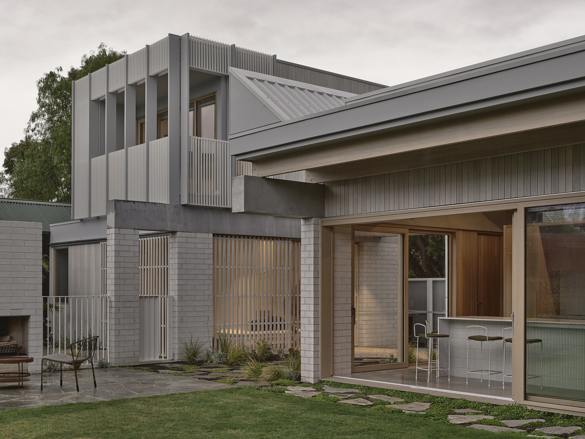 Rear courtyard showing the two-story corrugated metal volume above stacked brick walls at dusk