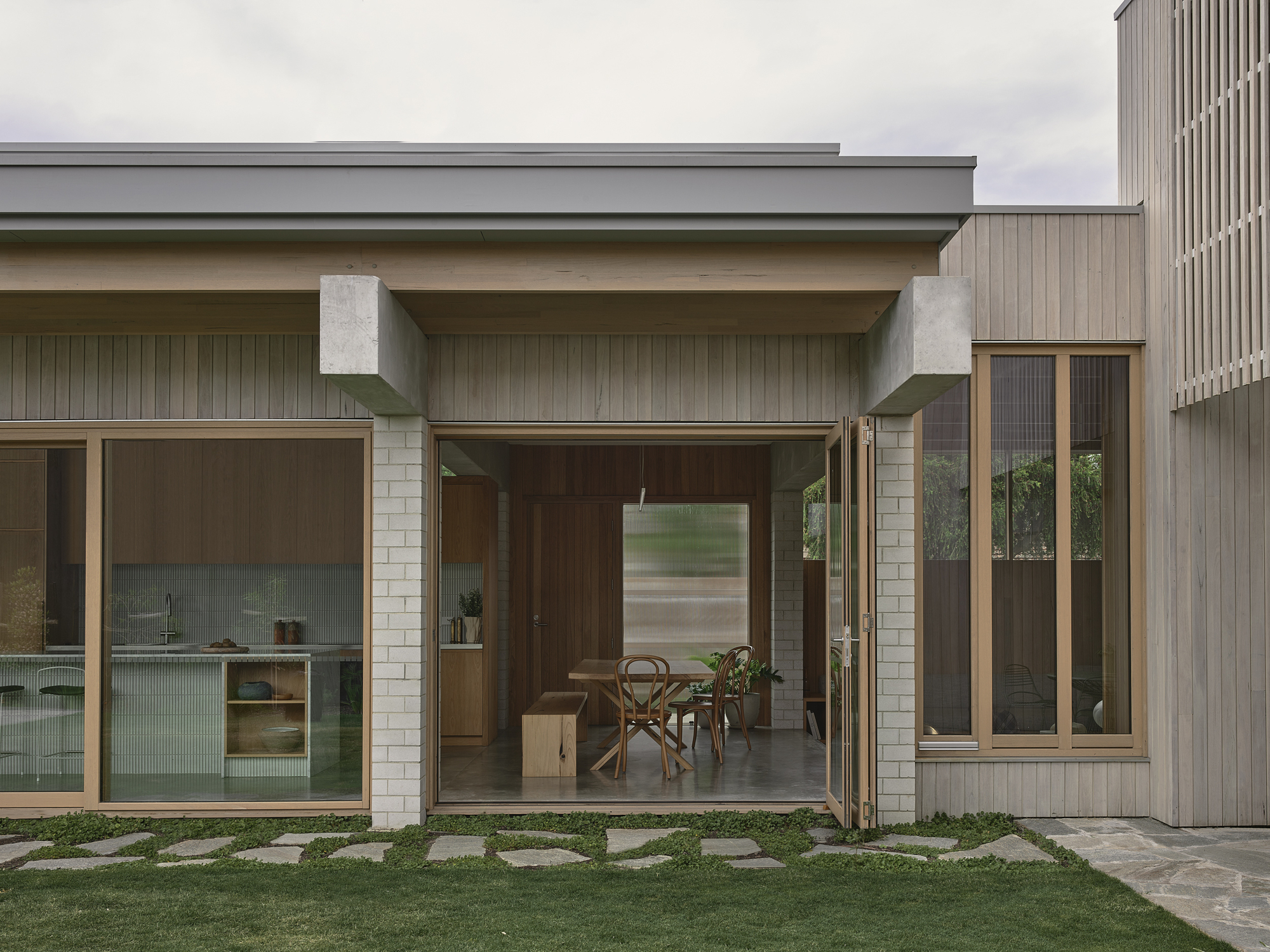 Rear facade with concrete beams sheltering glazed openings and stone paver path through lawn