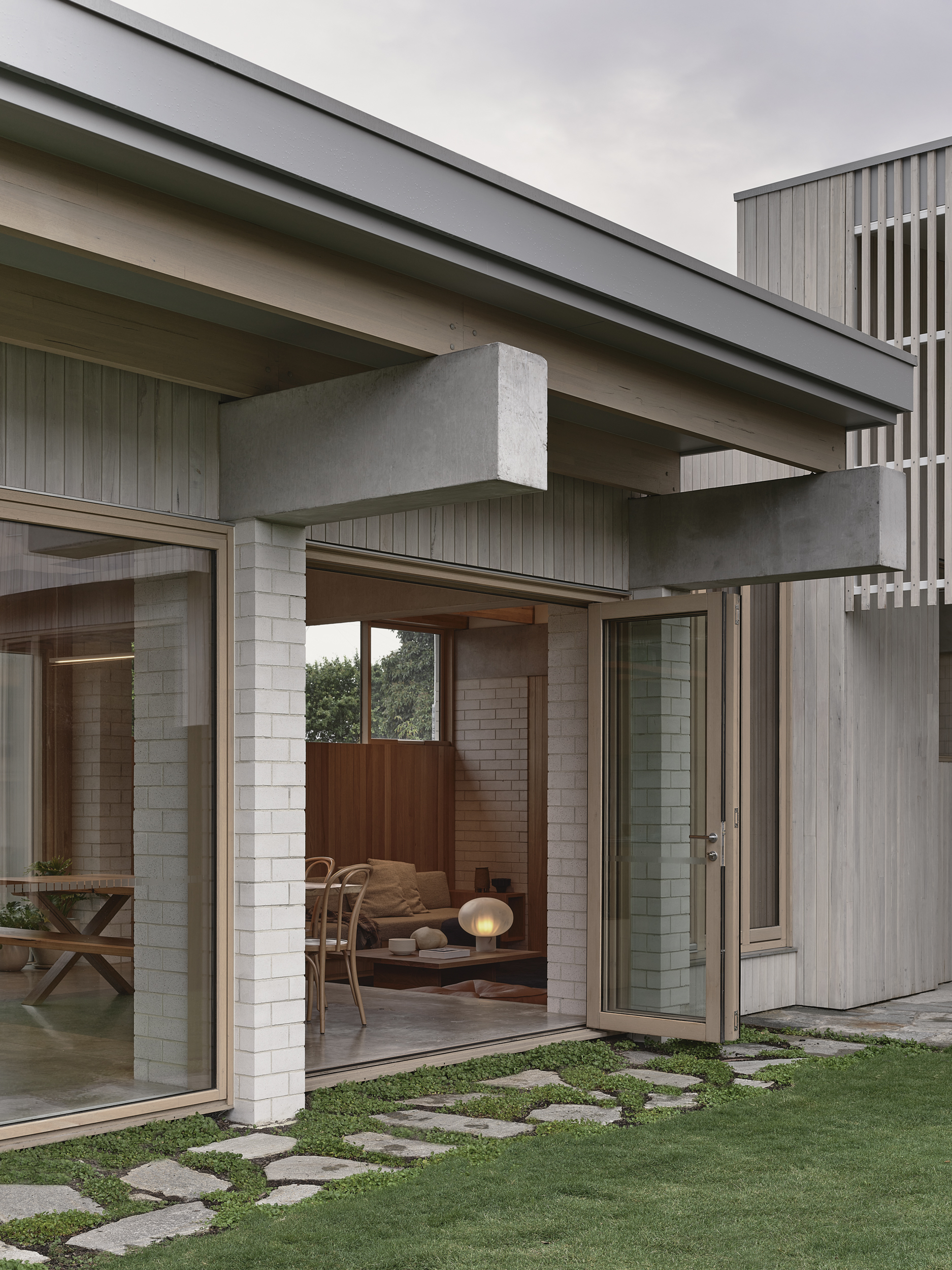 Covered terrace with exposed concrete beams and vertical timber cladding under an overcast sky