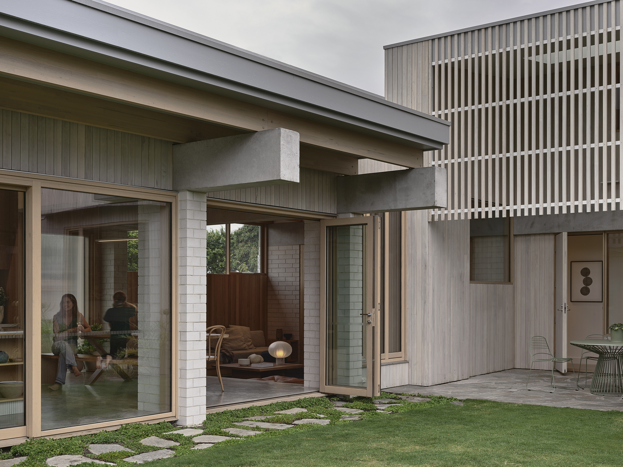 Glass-walled living area opening to a lawn courtyard with stepping stone path and residents inside