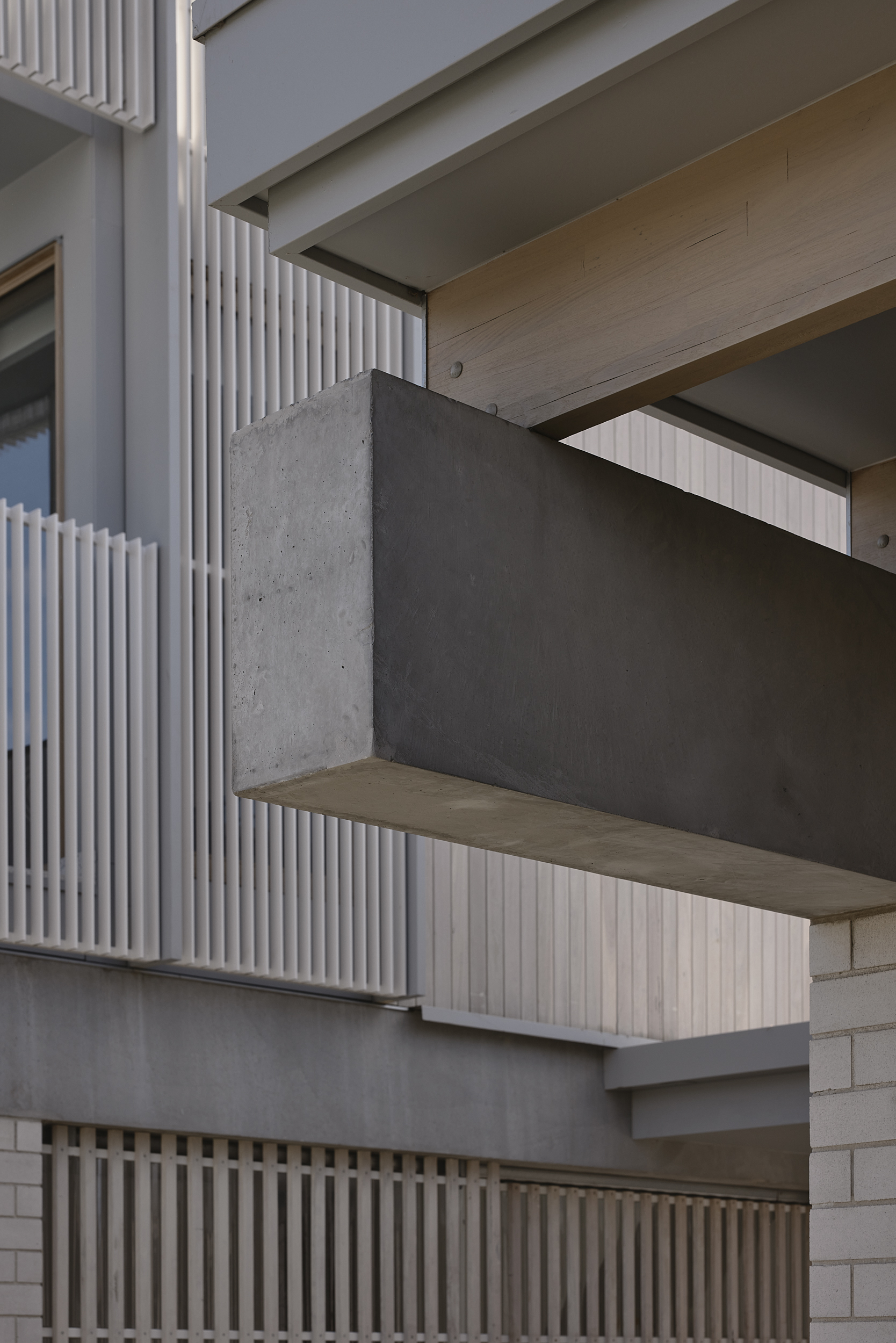 Close-up of cantilevered concrete balcony with timber soffit and vertical slatted screen above