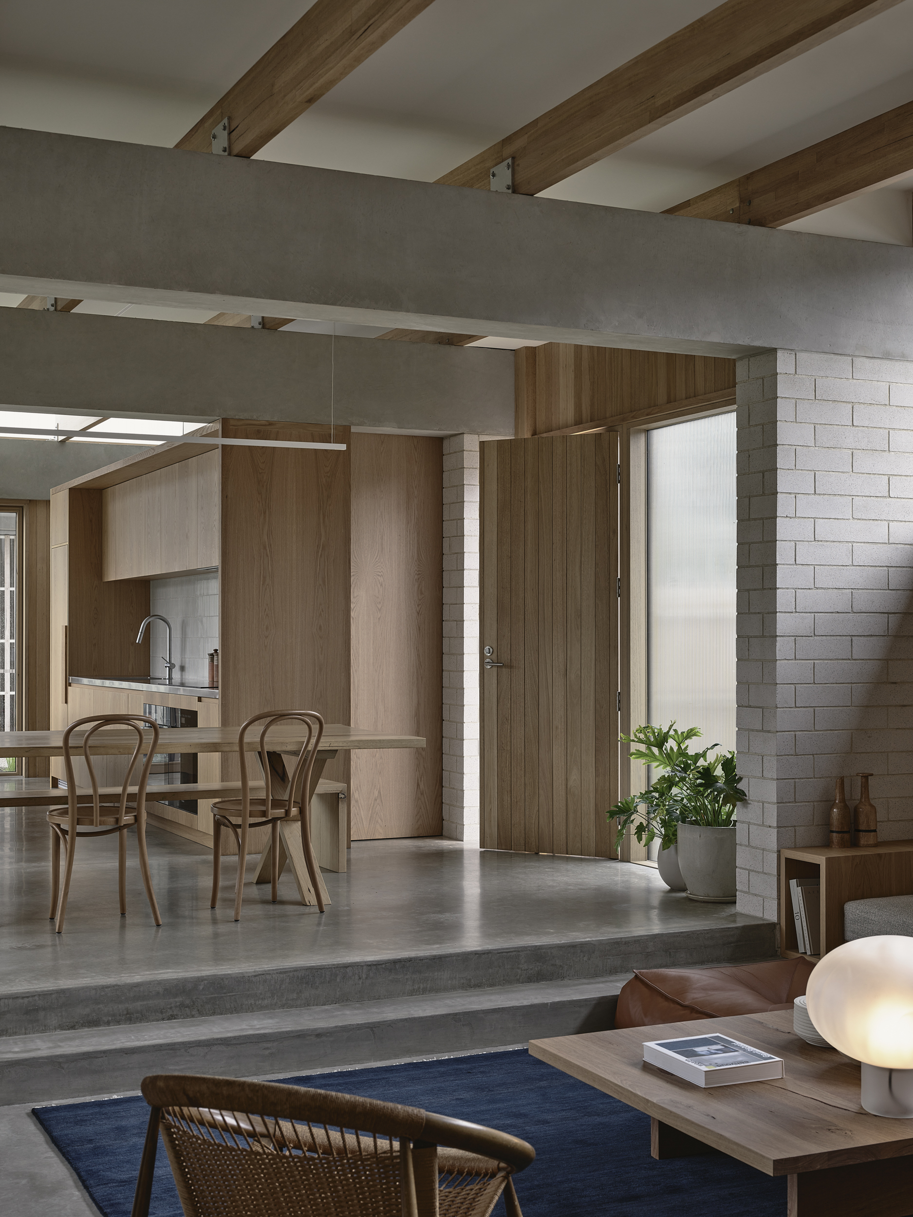 Interior view from living room toward raised dining area with exposed timber beams and white brick wall