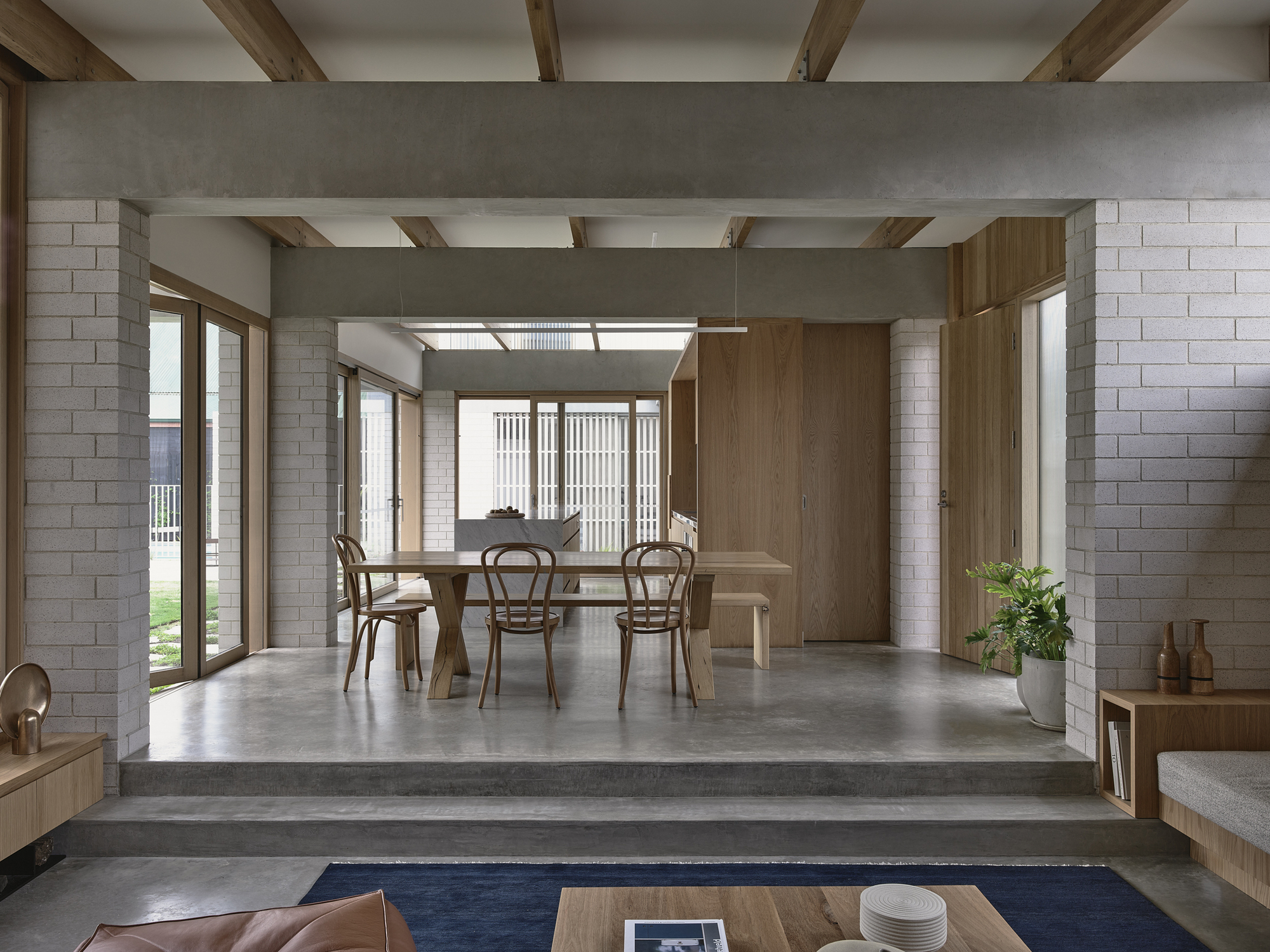 Dining area with timber table and chairs beneath exposed ceiling beams and vertical timber screen beyond