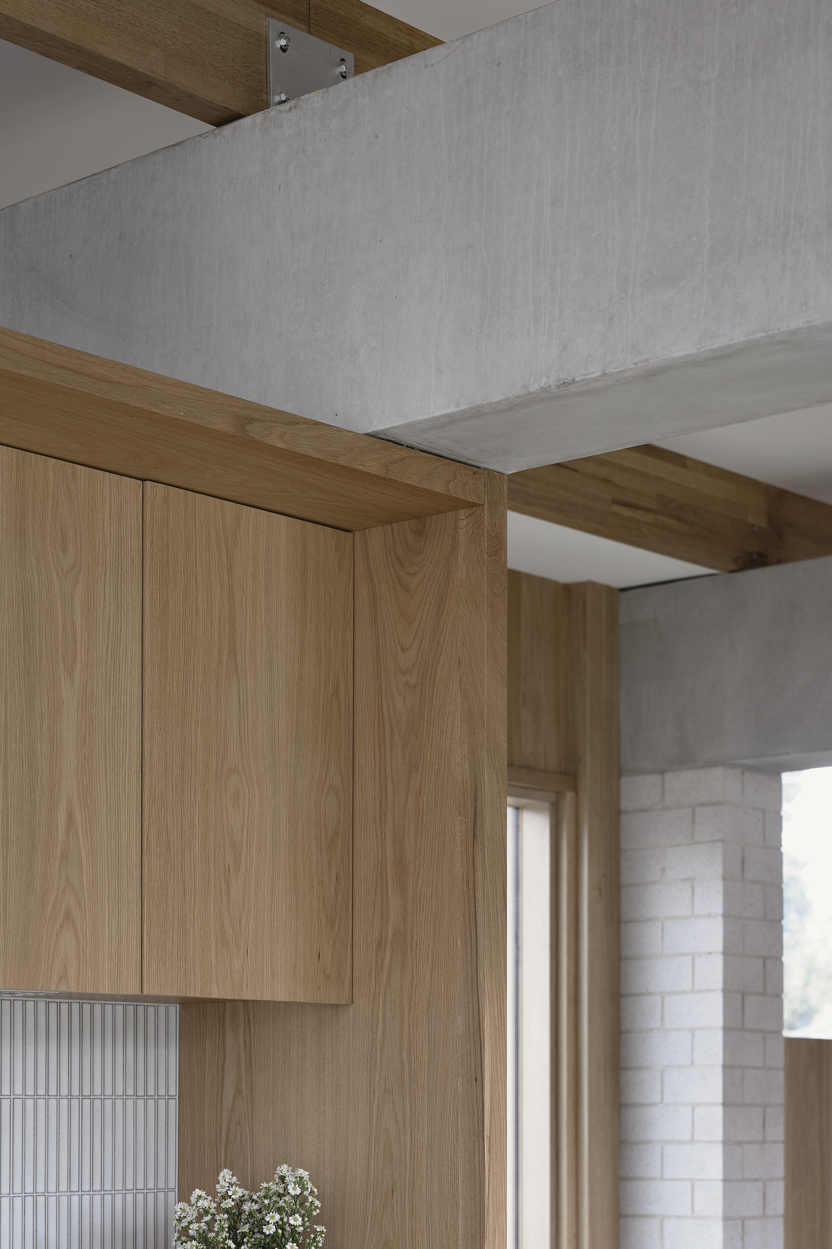 Detail of timber cabinetry meeting concrete beam with ribbed tile backsplash and white brick wall visible
