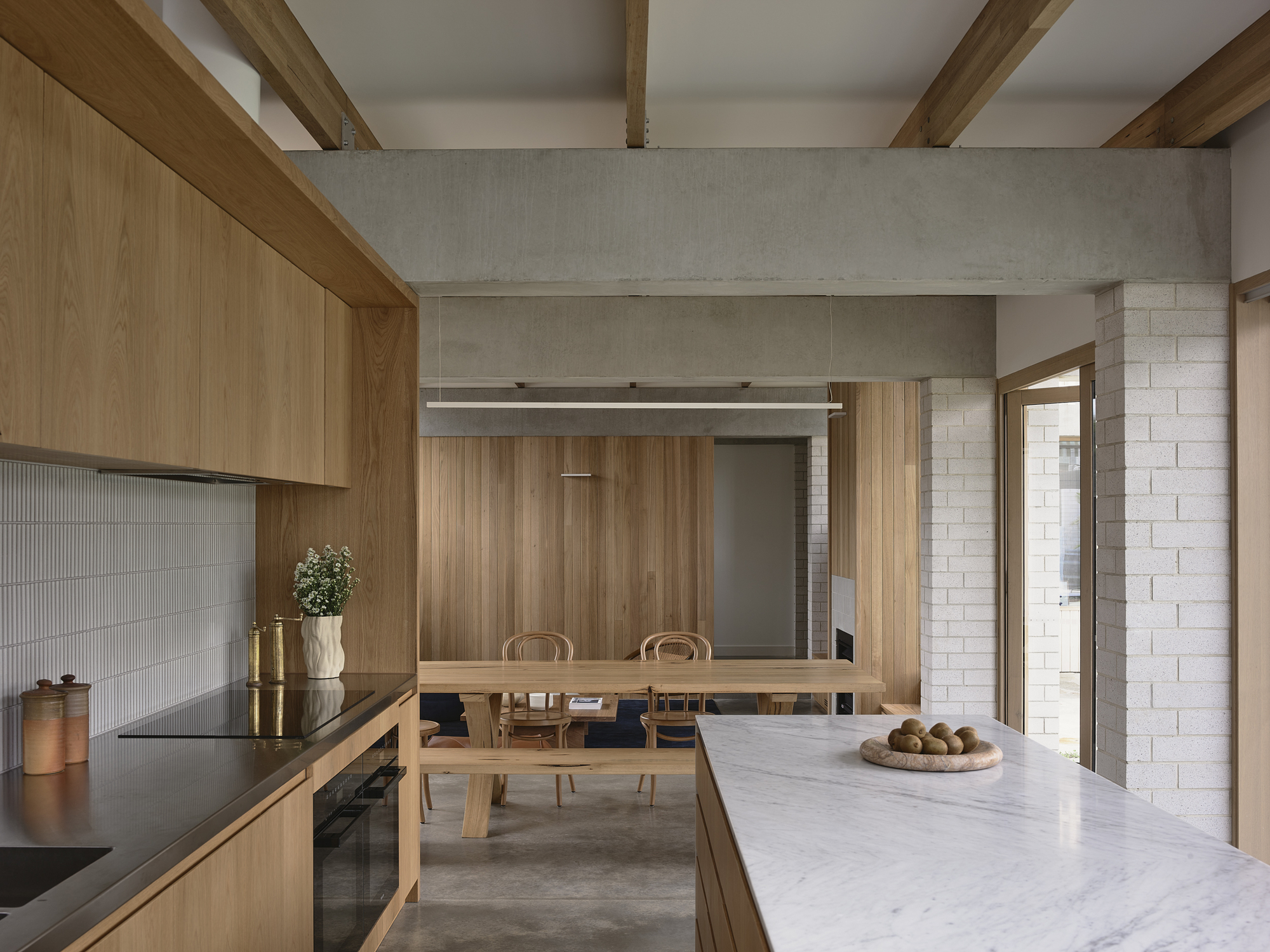 Kitchen with timber cabinetry, marble island, and view through to dining area with concrete beams overhead
