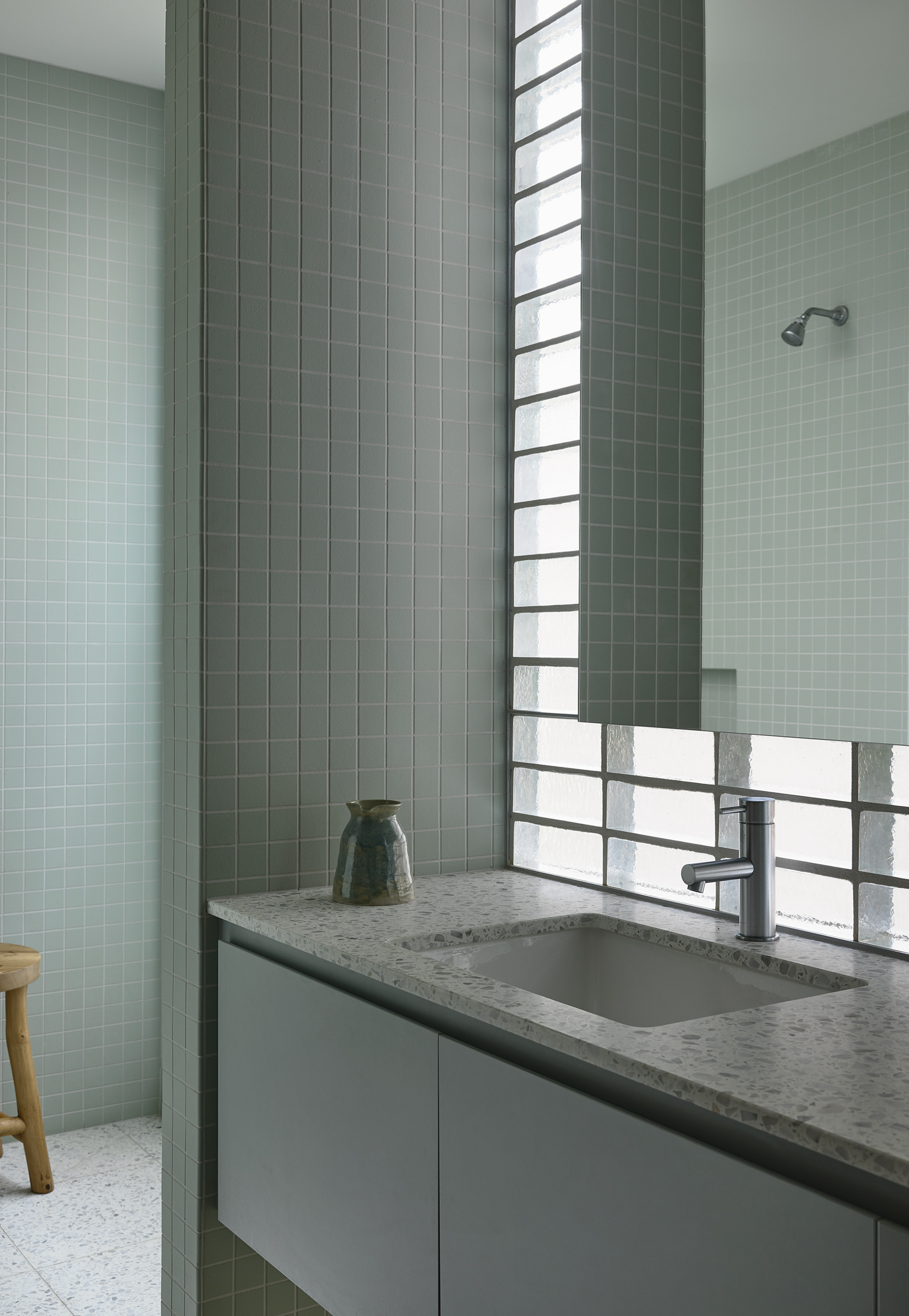 Vanity with terrazzo countertop beneath a horizontal glass block window flanked by sage green tile walls
