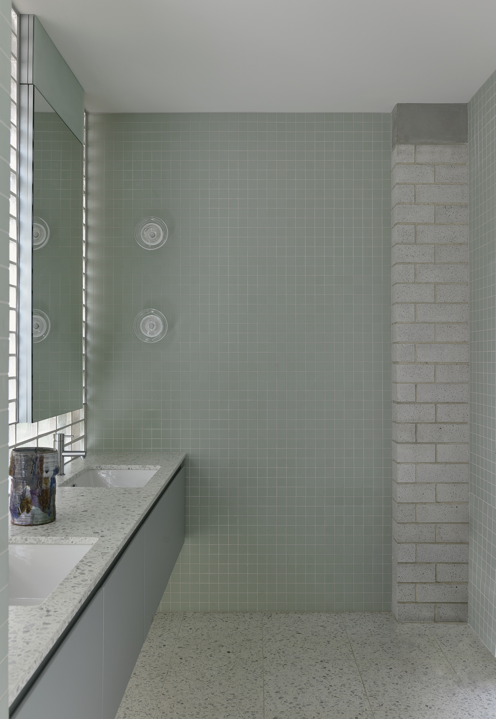 Shower area with sage green tile walls, rectangular glass block brick wall, and built-in wall fixtures