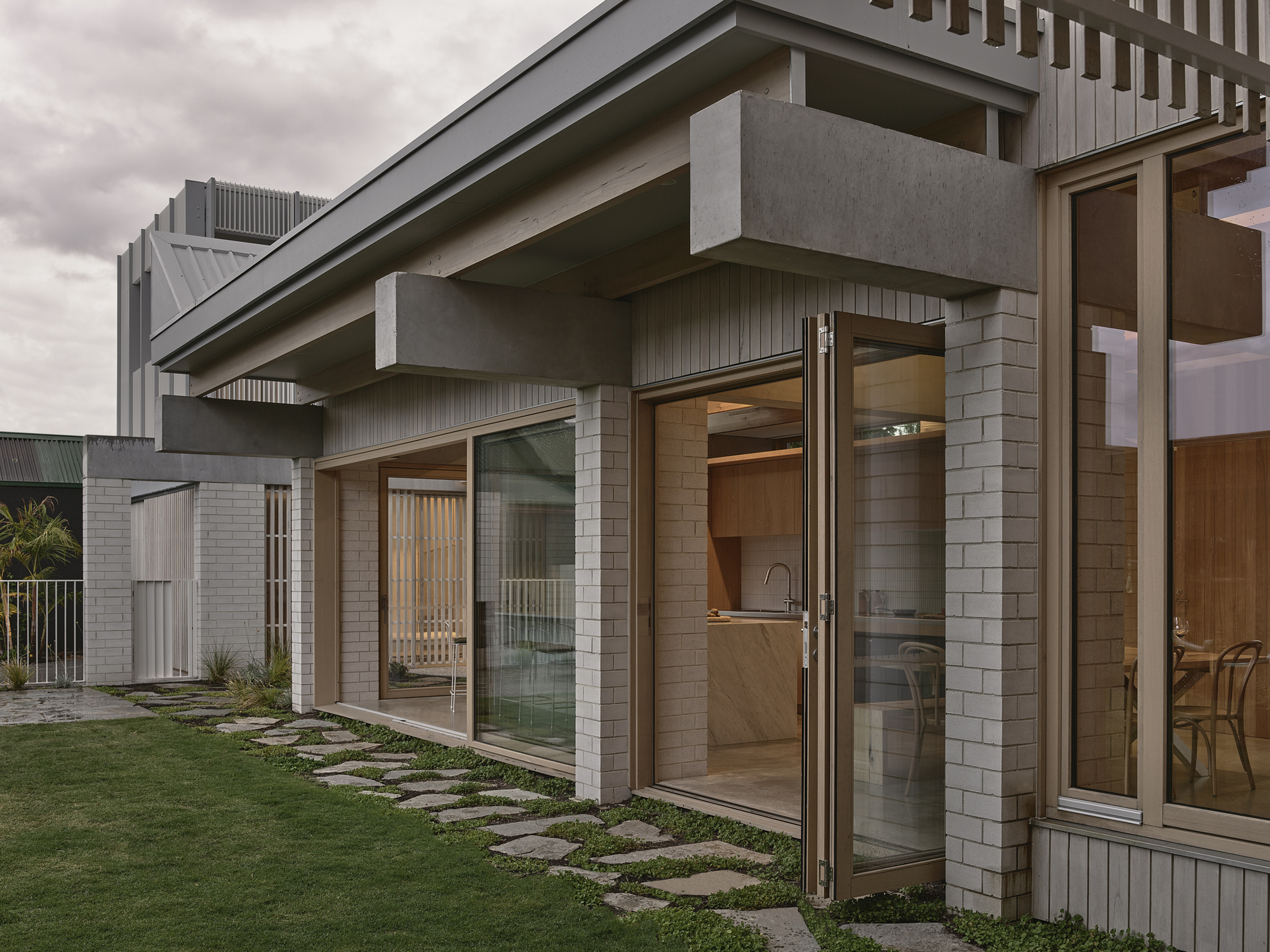 Close-up of cantilevered concrete beam over glazed doors with stepping stones through lawn