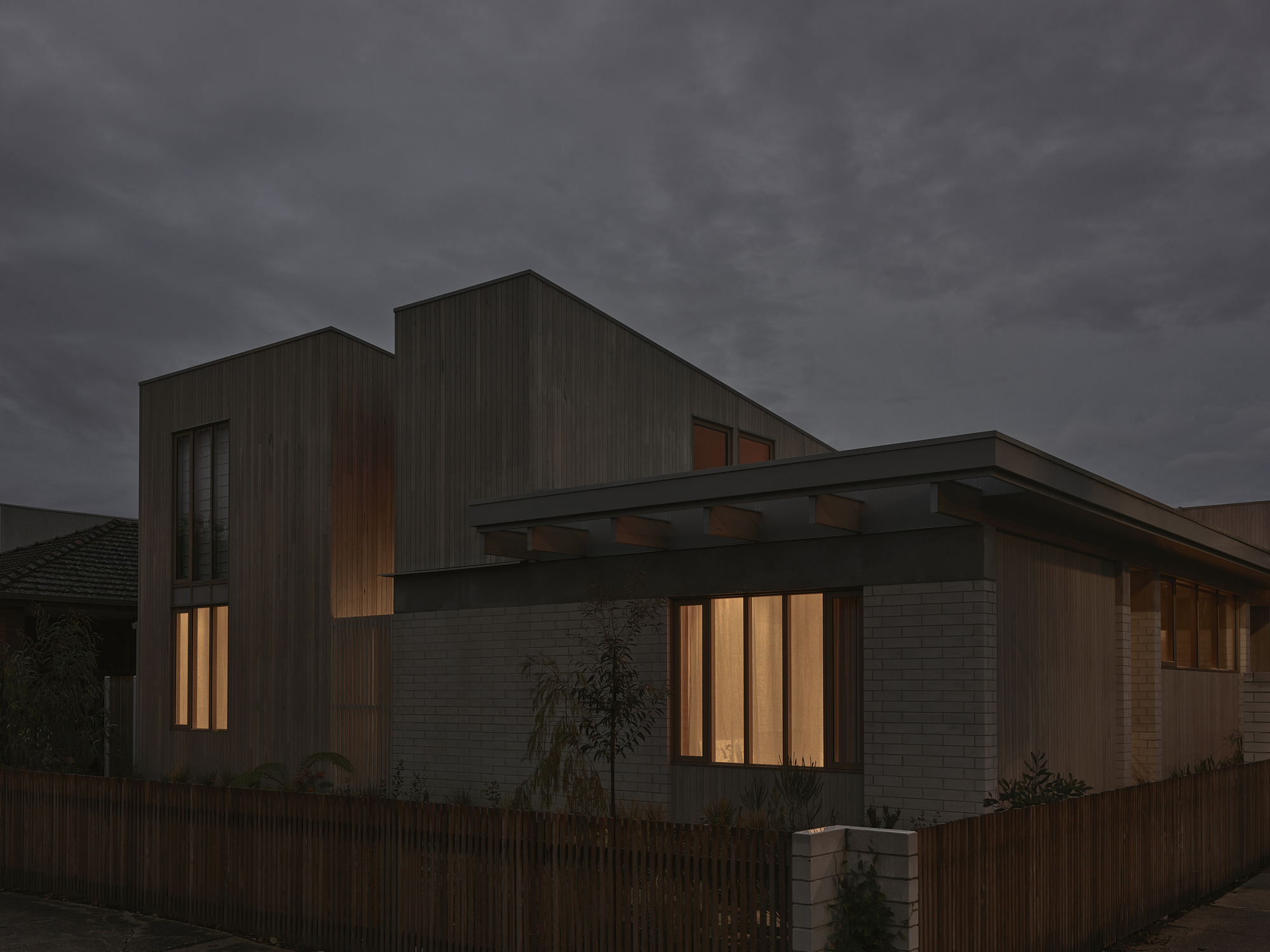 Street view of the timber-clad facade with vertical slatted windows glowing warmly at dusk