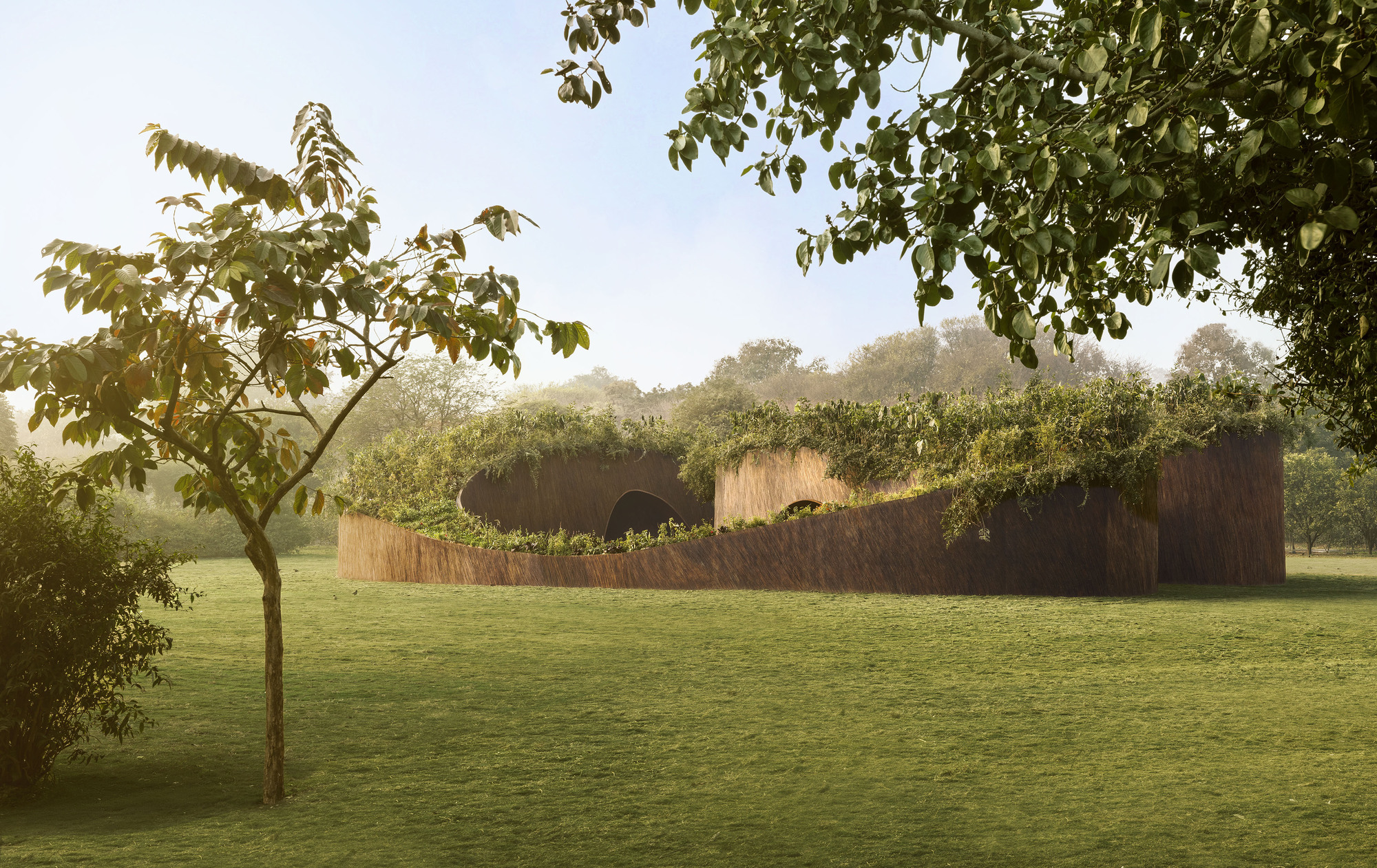 Curving rammed earth wall with planted green roof set in a mowed lawn under morning light