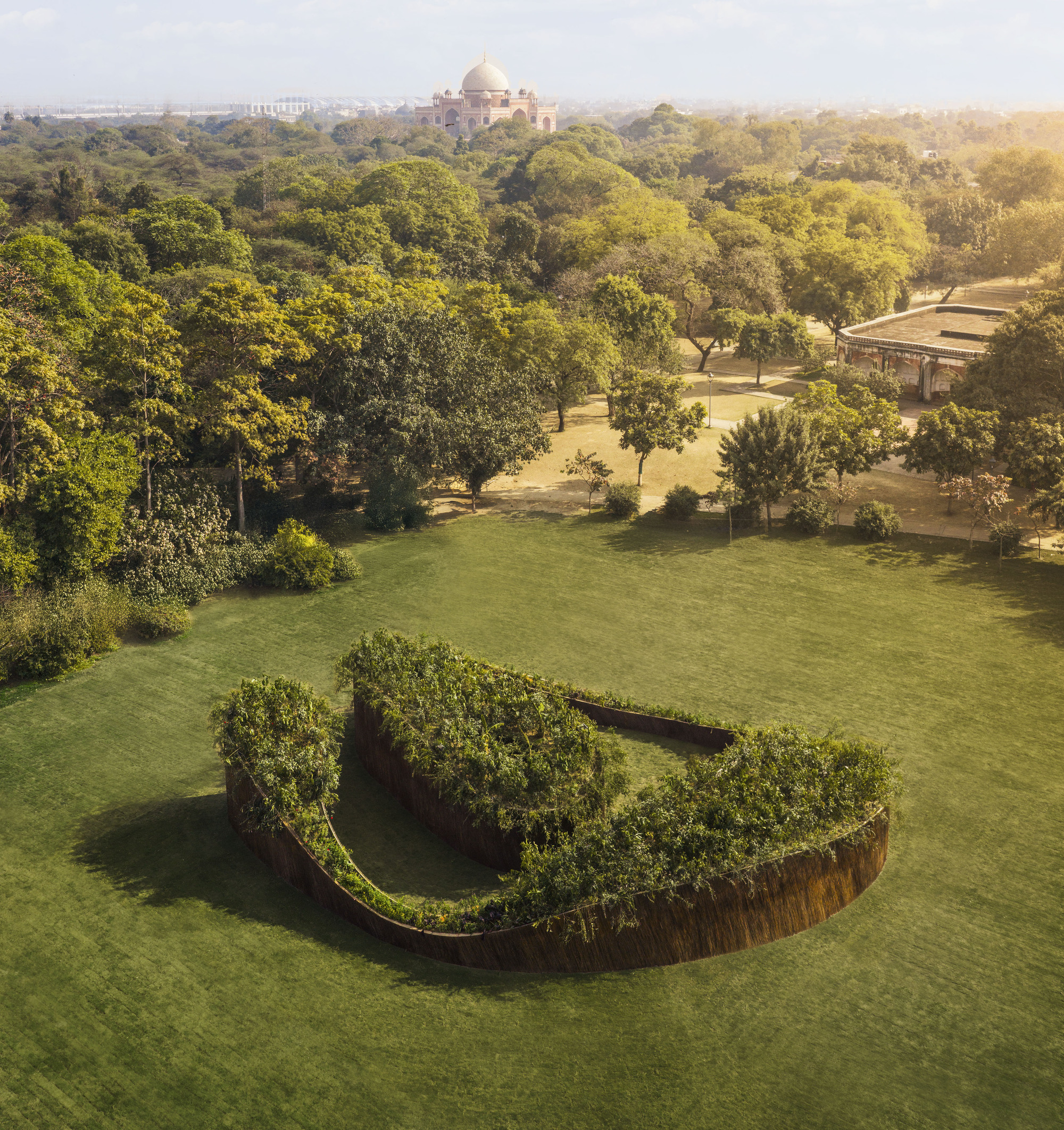 Aerial view of the spiral green-roofed structure in parkland with distant dome visible through haze