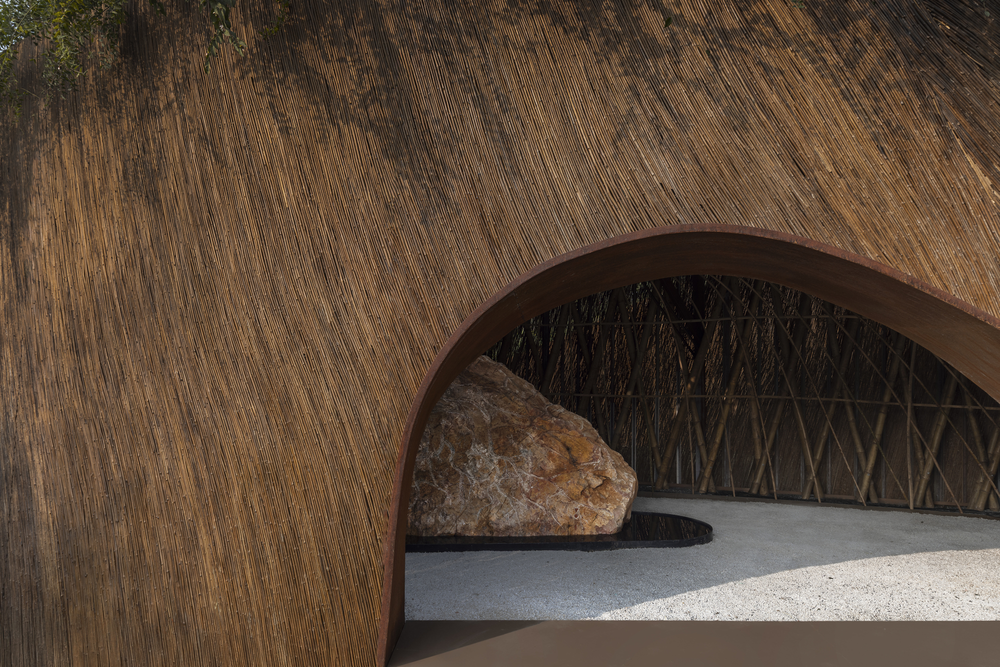 Close-up of the rammed earth arch framing bamboo lattice screen and stone in gravel courtyard