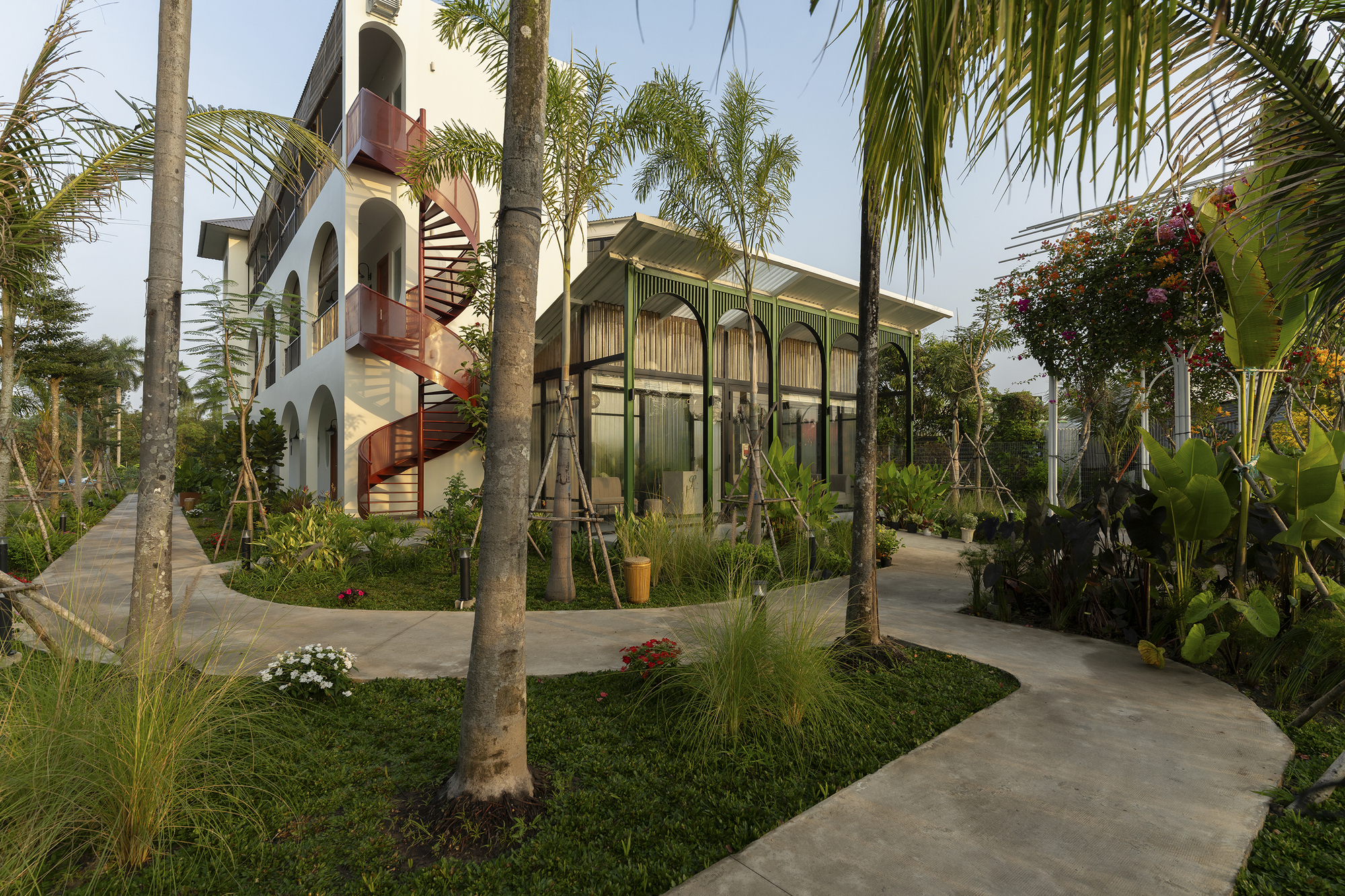 Garden pathways winding through palm trees toward the screened pavilion and residential block