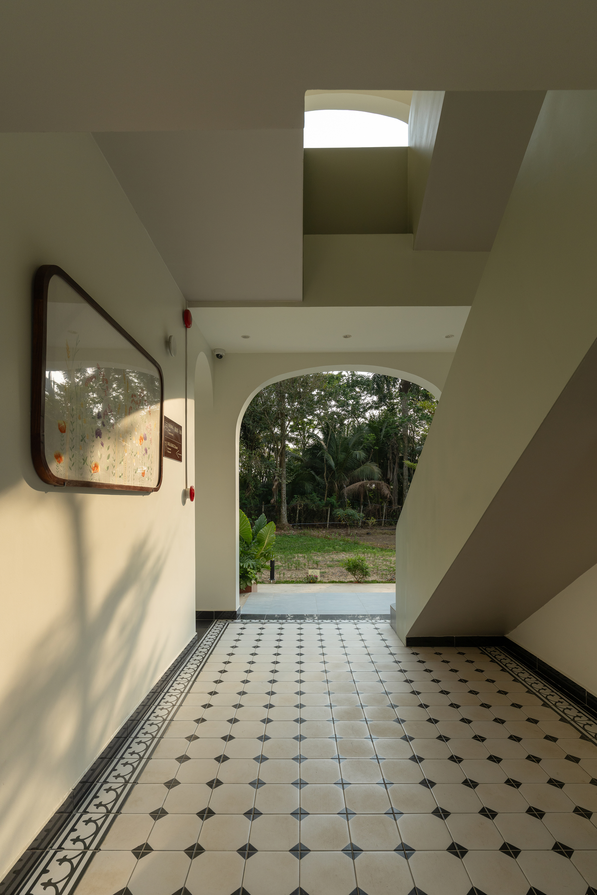 Entry hall with patterned tile floor and arched opening framing tropical vegetation beyond under skylight